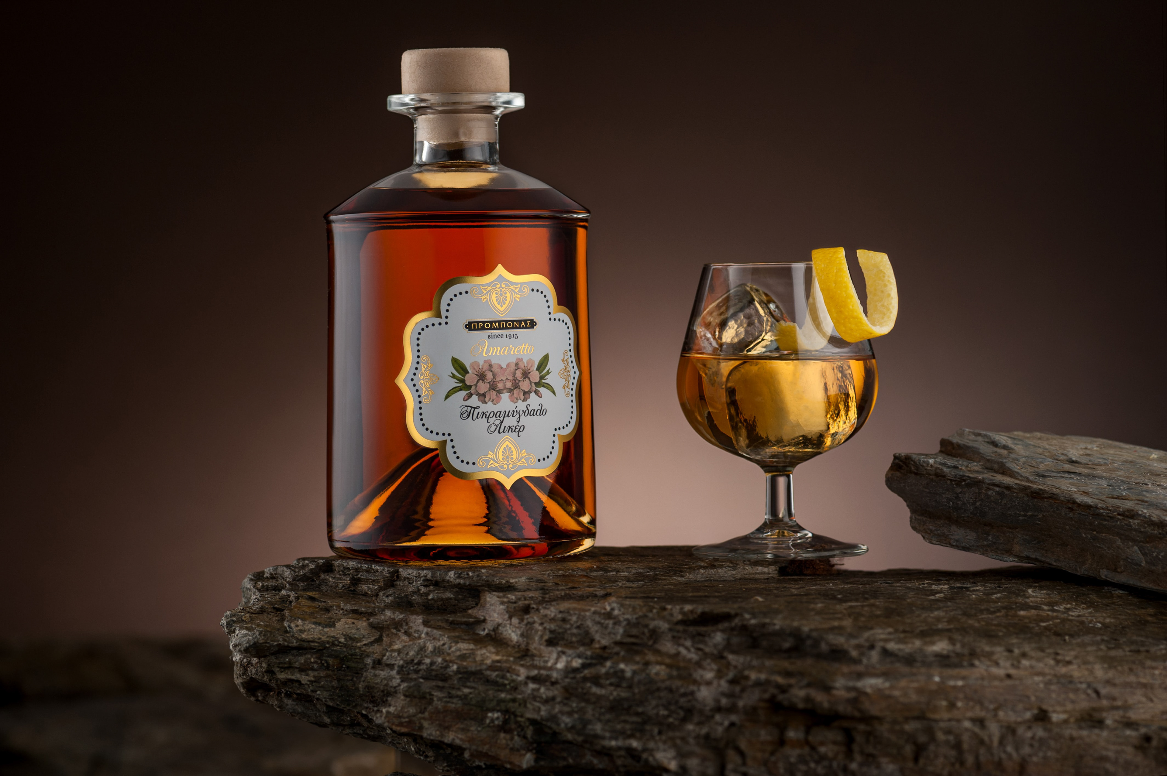 διαφημιστική φωτογράφηση φιάλης λικέρ Amaretto πάνω σε πέτρα με ποτήρι και λεμόνι για προώθηση , advertising photography of a bottle of Amaretto liqueur on a stone with a glass and lemon for promotion