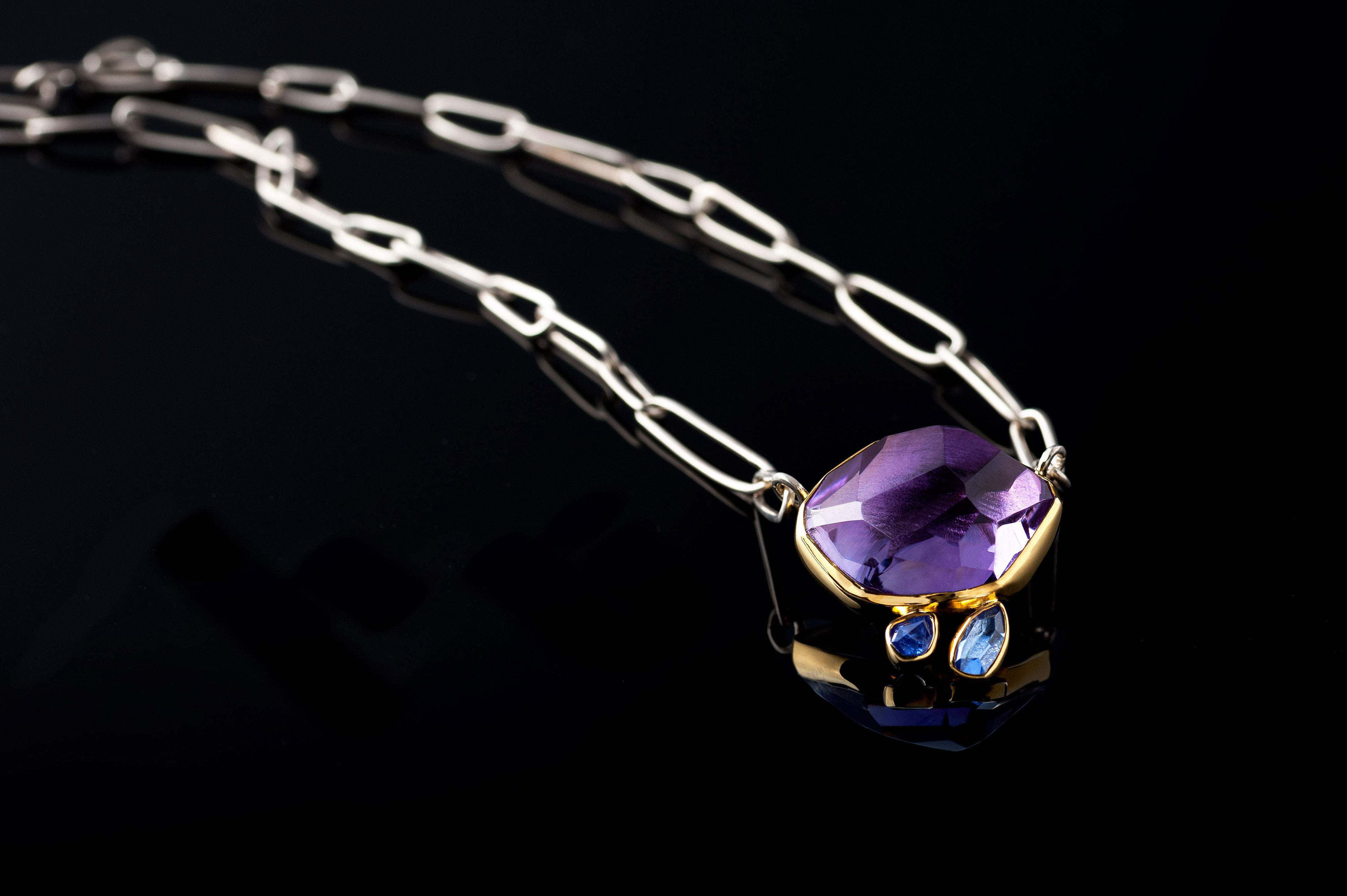 Margoni jewellery: επίχρυσο μενταγιόν με μώβ ημιπολύτιμη πέτρα και ασημένια αλυσίδα σε μαύρο φόντο με ανανάκλαση