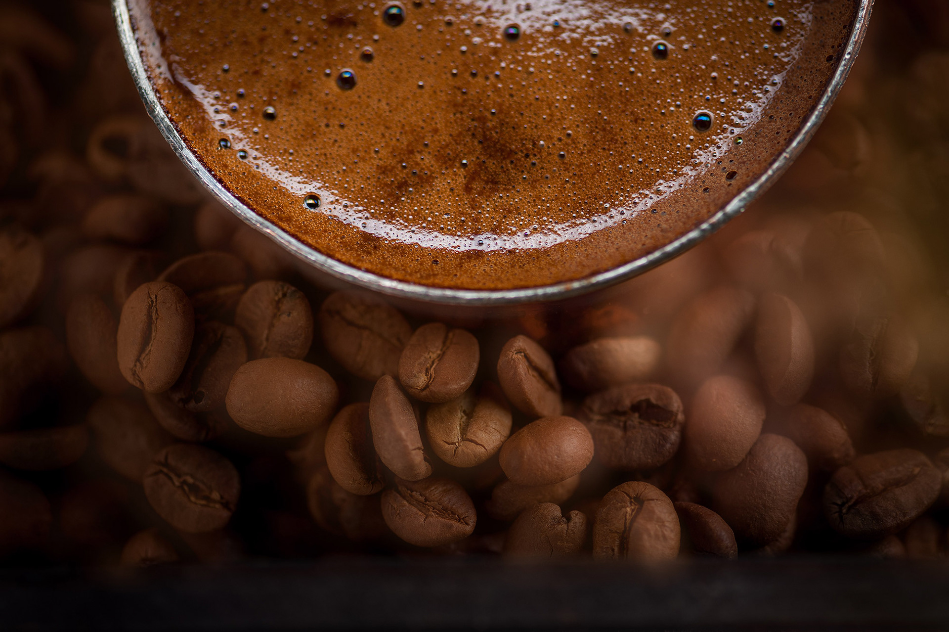 Μια εντυπωσιακή, κοντινή macro φωτογραφία fine art food photography, όπου το πλούσιο, χρυσαφένιο καϊμάκι του ελληνικού καφέ έρχεται σε τέλεια αντίθεση με τους καβουρδισμένους κόκκους που βρίσκονται στο υπόβαθρο, από τη φωτογράφο Βούλα Γκώτη. An exquisite macro fine art food photography piece capturing the rich, golden foam of traditional Greek coffee, beautifully contrasted against textured roasted coffee beans in the background, by photographer Voula Gkoti.