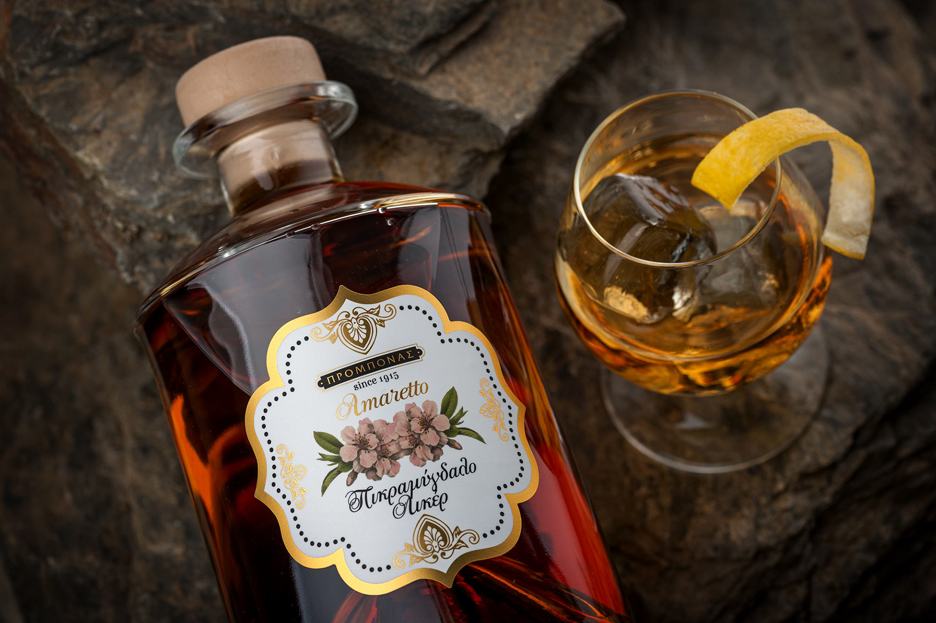 κοντινό πλάνο από πάνω μπουκάλι amaretto με ποτήρι δίπλα πάνω σε πέτρα 