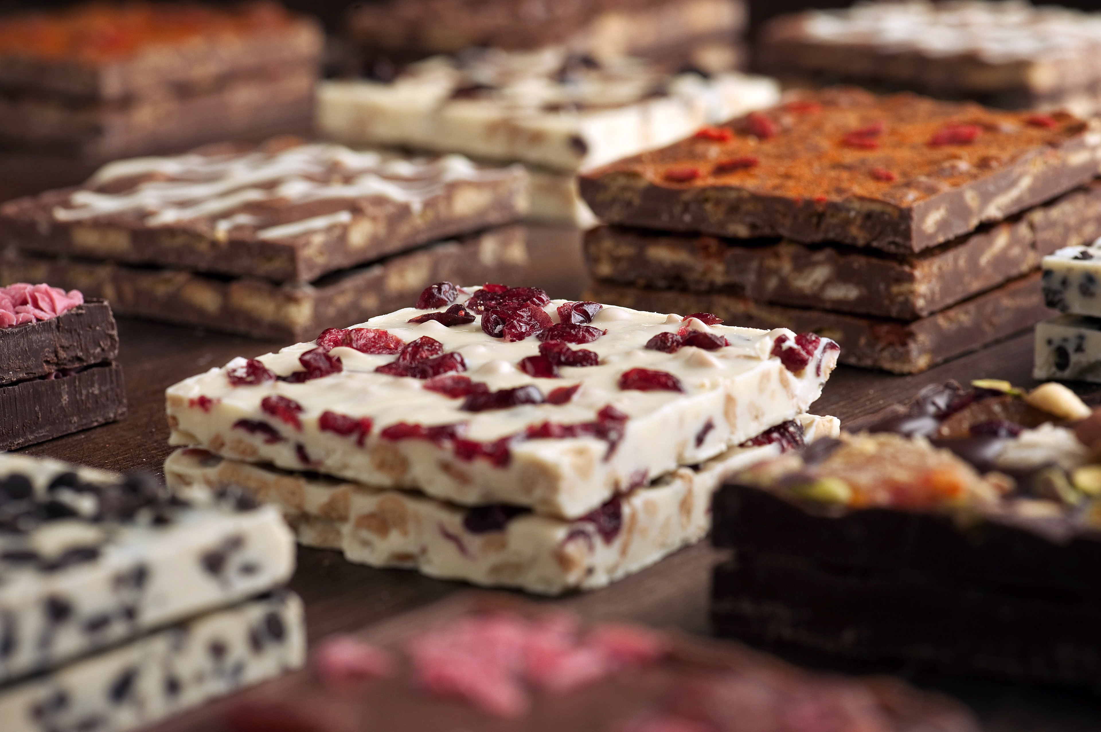 voula gkoti photography various of hand made chocolates on a wood tasty bites with peanut butter, bralina and coconut by laurence-galerie de chocolat