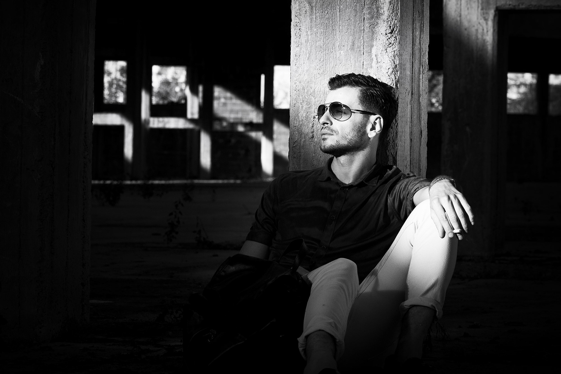 Πορτραίτο άνδρα καθισμένου στο πάτωμα με έντονες σκιές και φως να διαπερνά τον χώρο.    Portrait of a man sitting on the ground with dramatic light and shadow interplay in an abandoned space.