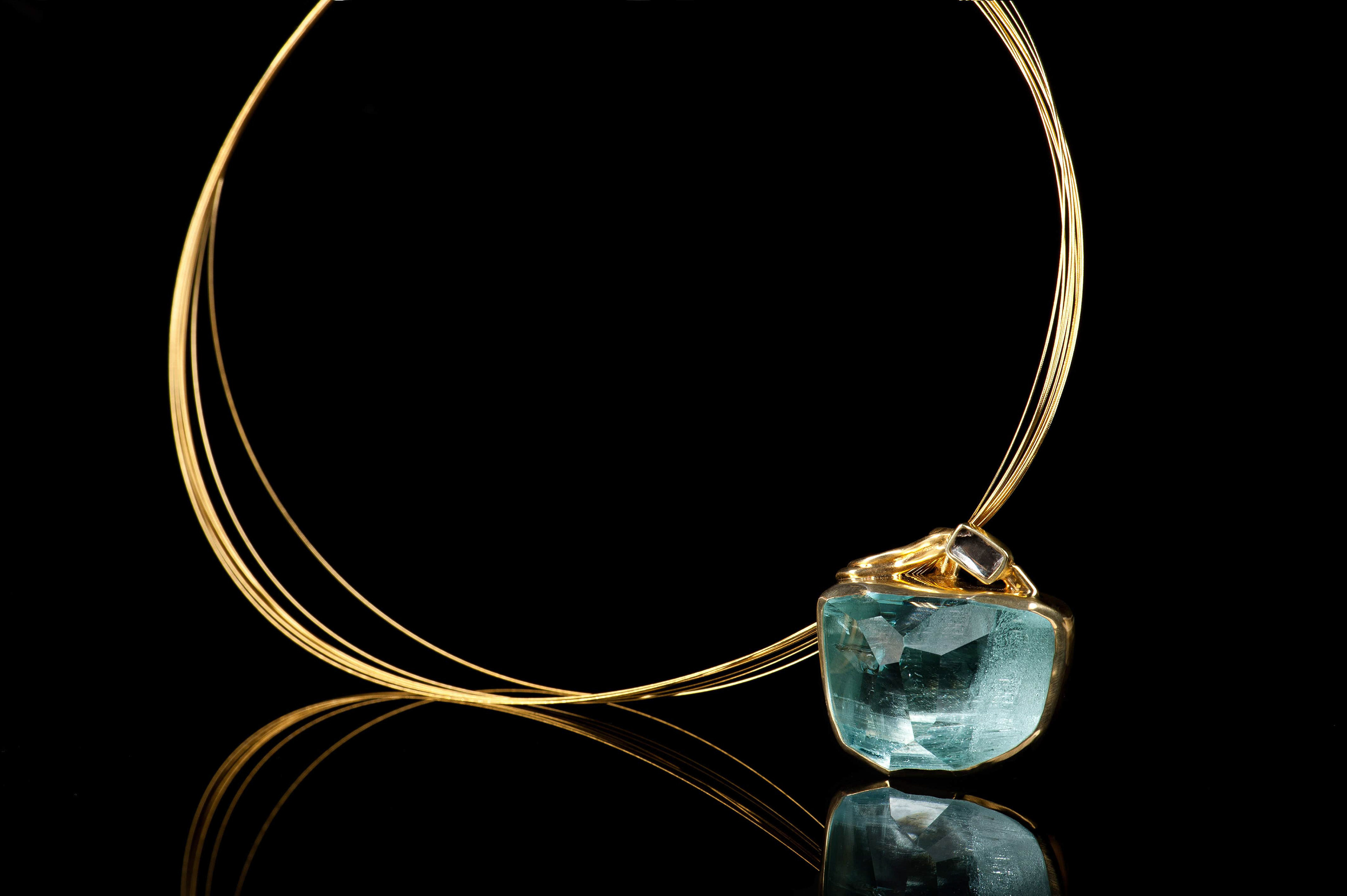 Margoni jewellery: επίχρυσο μενταγιόν με γαλάζιο πετράδι και αέρινη αλυσίδα σε μαύρο φόντο με ανανάκλαση