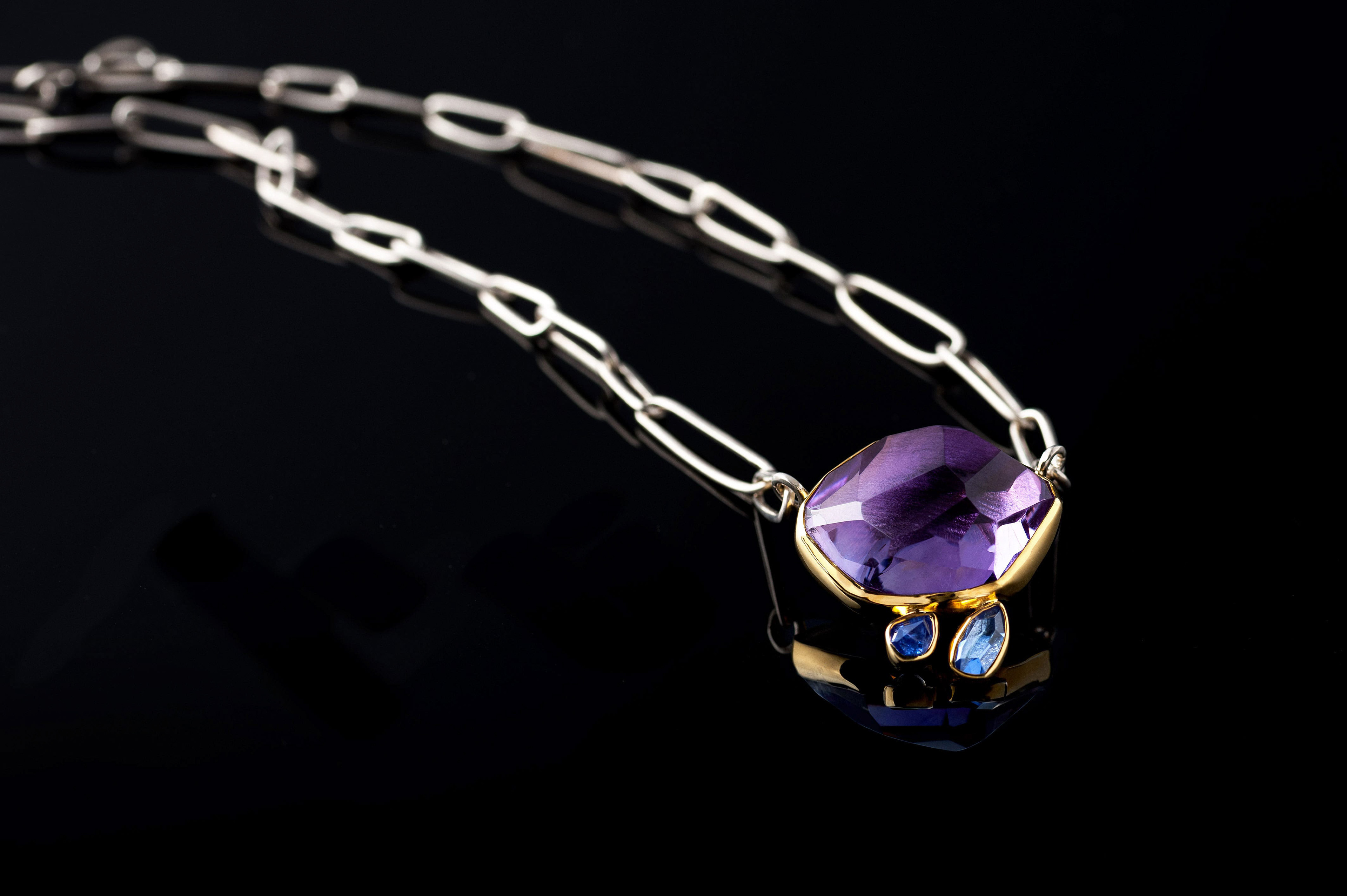 Margoni jewellery: επίχρυσο μενταγιόν με μώβ ημιπολύτιμη πέτρα και ασημένια αλυσίδα σε μαύρο φόντο με ανανάκλαση