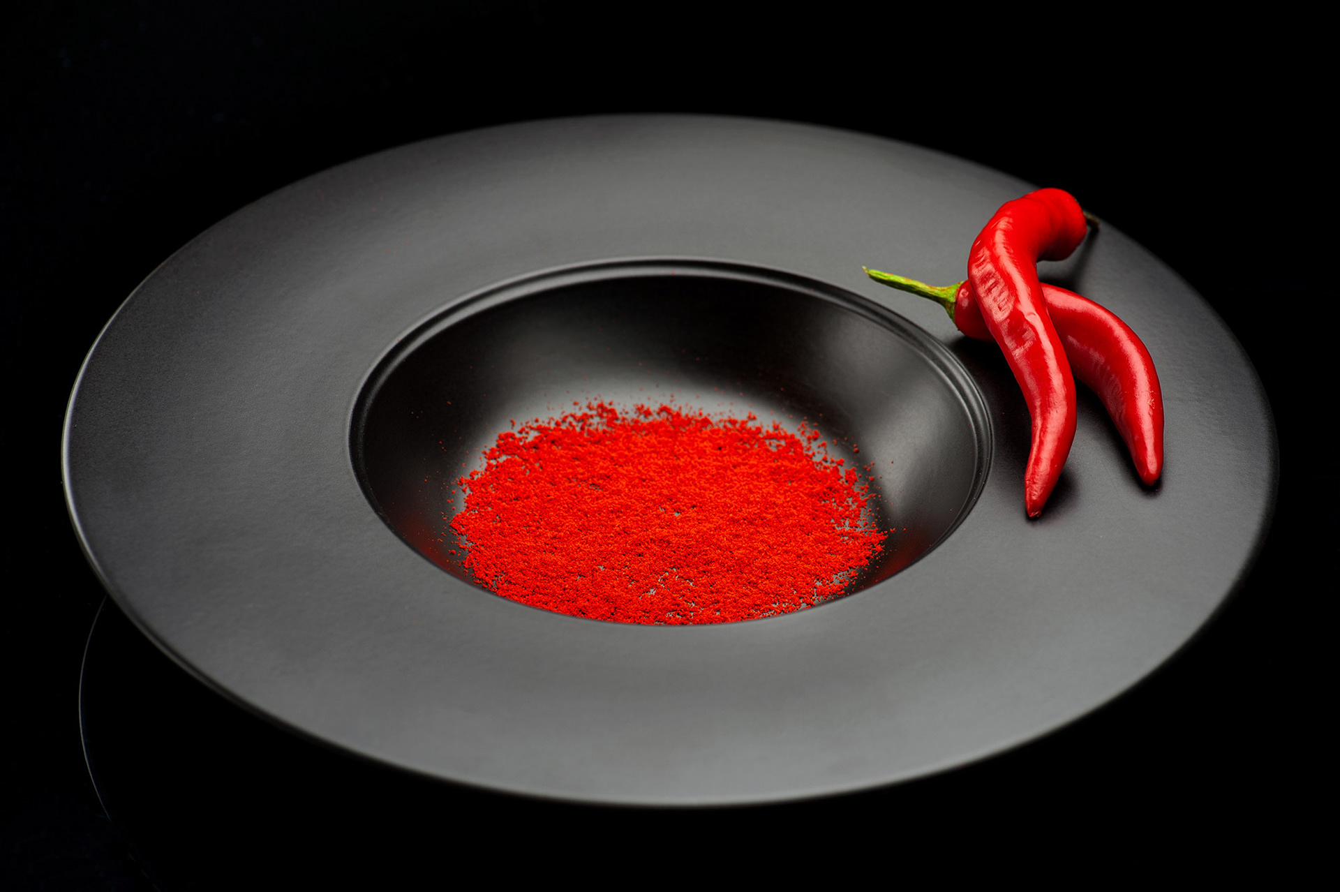 Σύνθεση πιάτου με μπαχαρικά chilli σε σκόνη και πιπεριές σε μαύρο πιάτο και μαύρο φόντο, clean minimal background