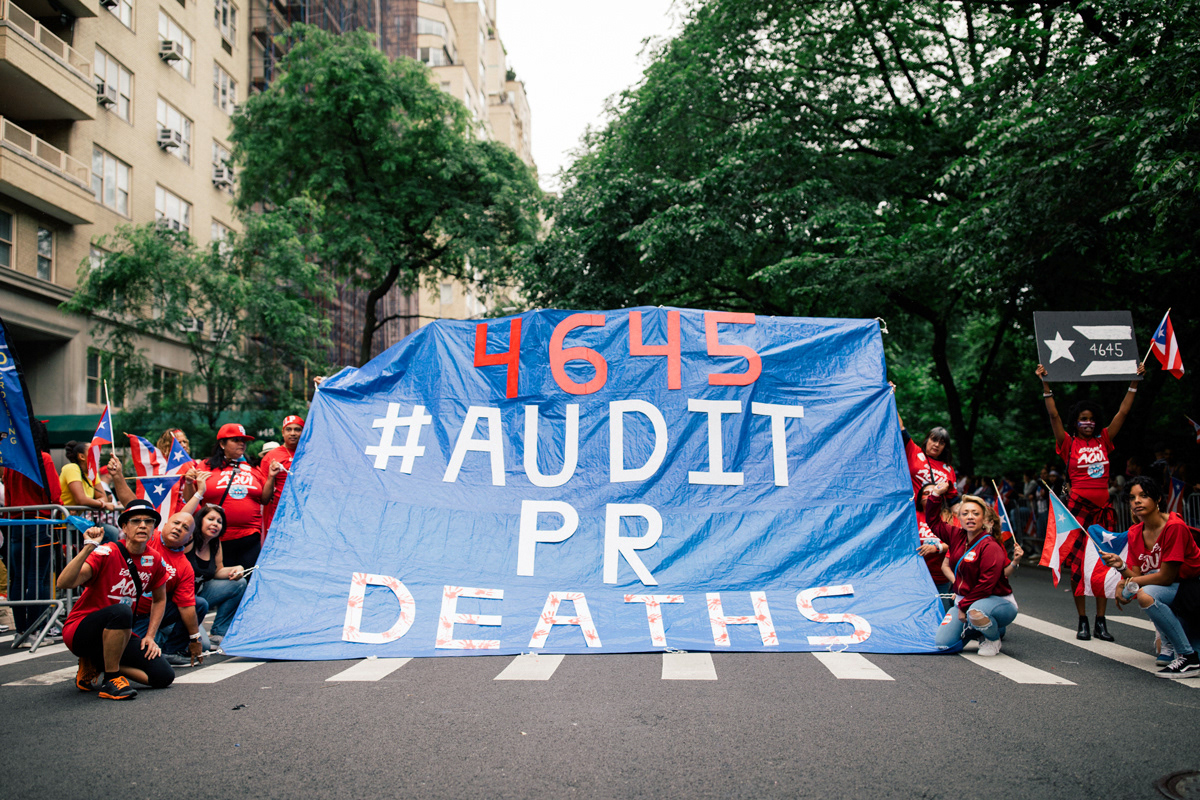 Marchers stop the parade briefly to hold open a large tarp displaying the midpoint of the newly released death toll estimates on Fifth Avenue and East 76th Street.
