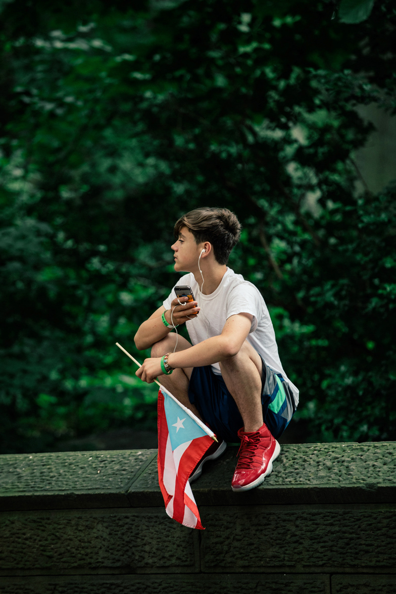 A young teen perches on the walls that surround Central Park to watch the parade.