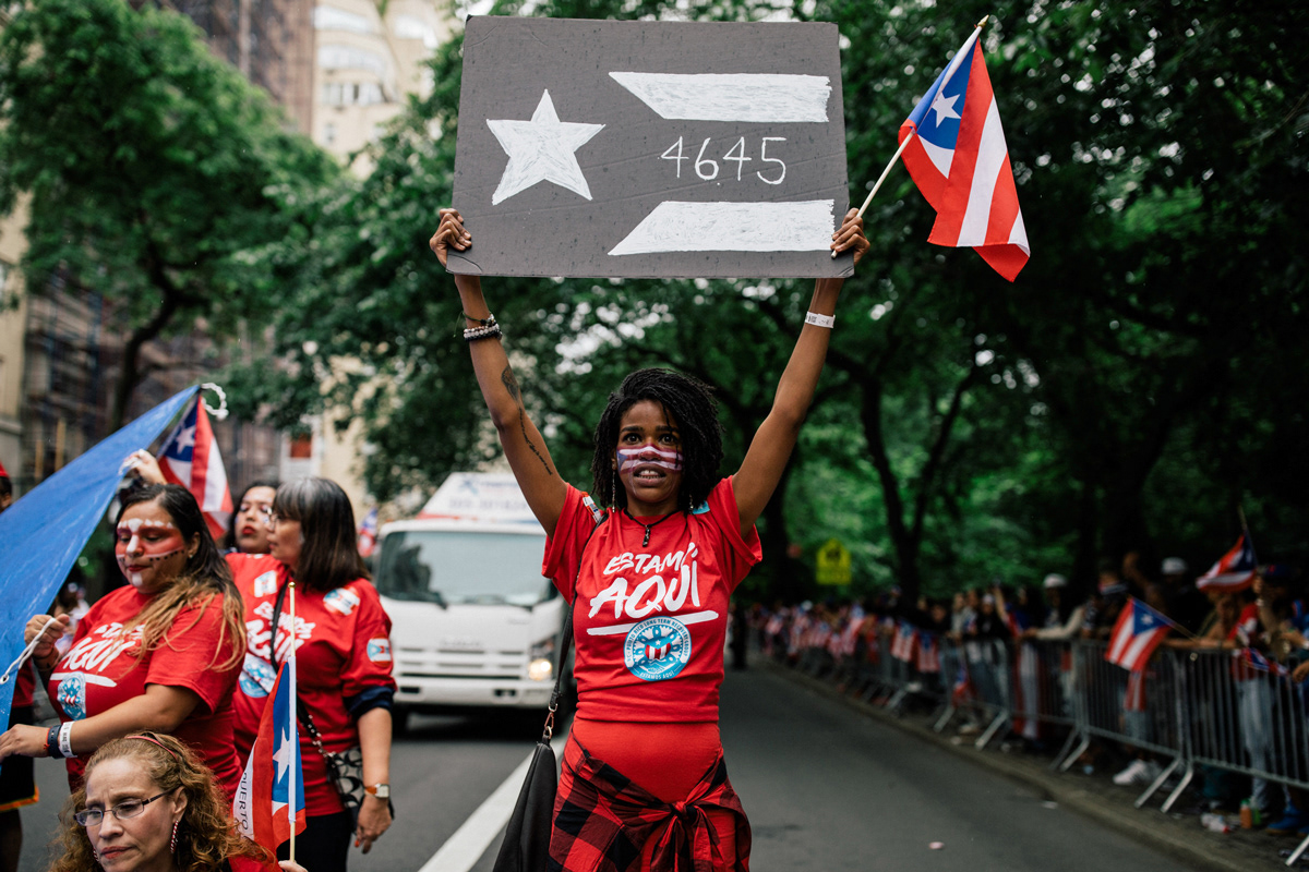 A marcher holds a sign displaying the numbers “4645,” referencing a recent study on the deaths caused by Hurricane Maria, at Fifth Avenue and East 76th Street.