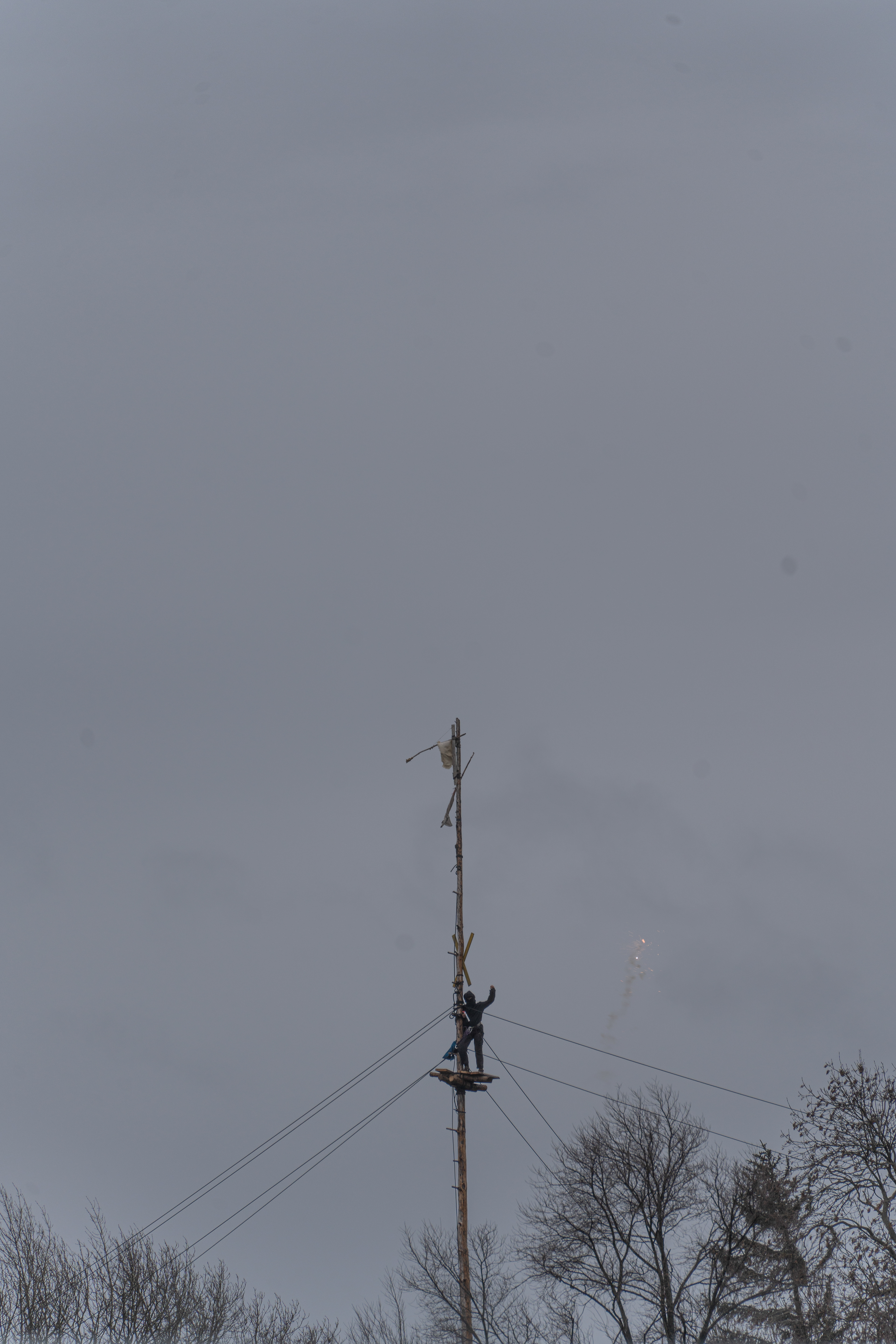 Ein Mensch aus der Besetzung klettert einen Mast hoch um der Demo auf der anderen Seite des Zaunes zu signalisieren