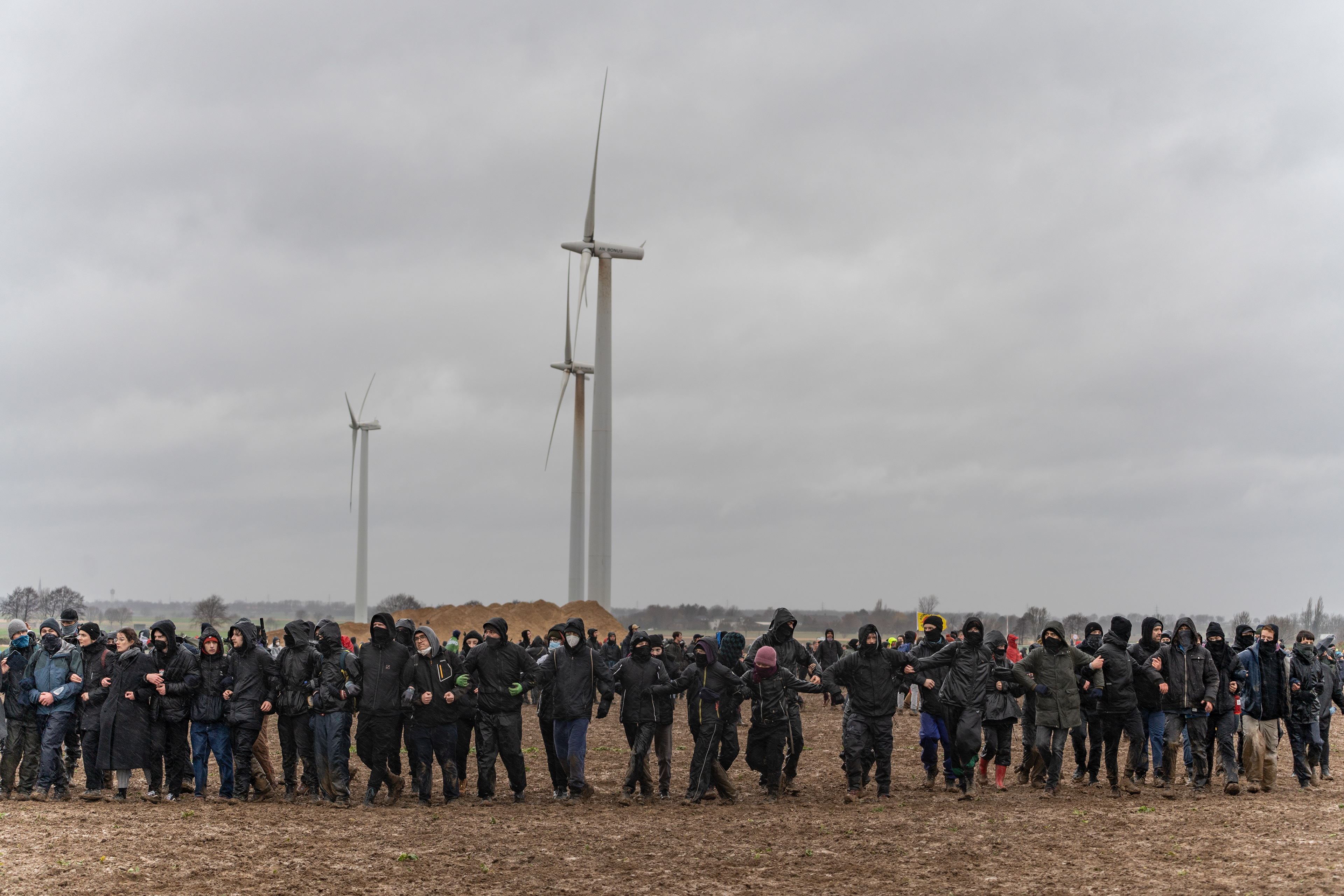 Eine Kette Demonstrant*innen laufen eingehakt über ein Feld