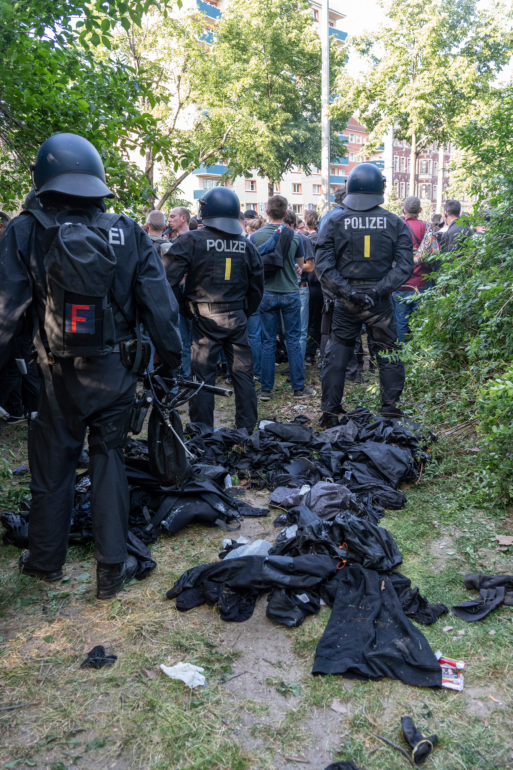 Polizist*innen stehen vor einem Haufen abgelegter schwarzer Klamotten.