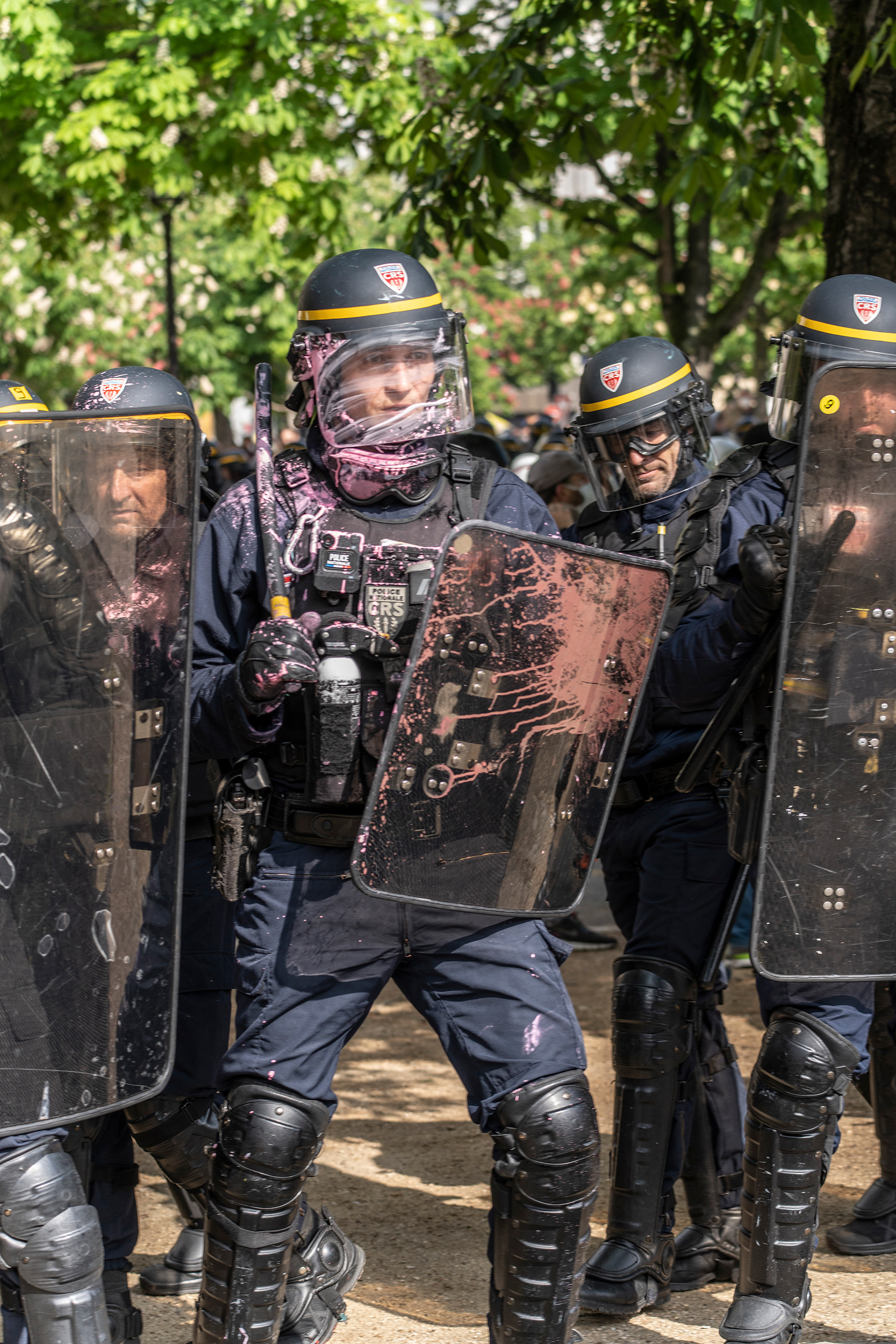 Ein farbbeschmierter Polizist steht neben seinen Kolleg*innen.