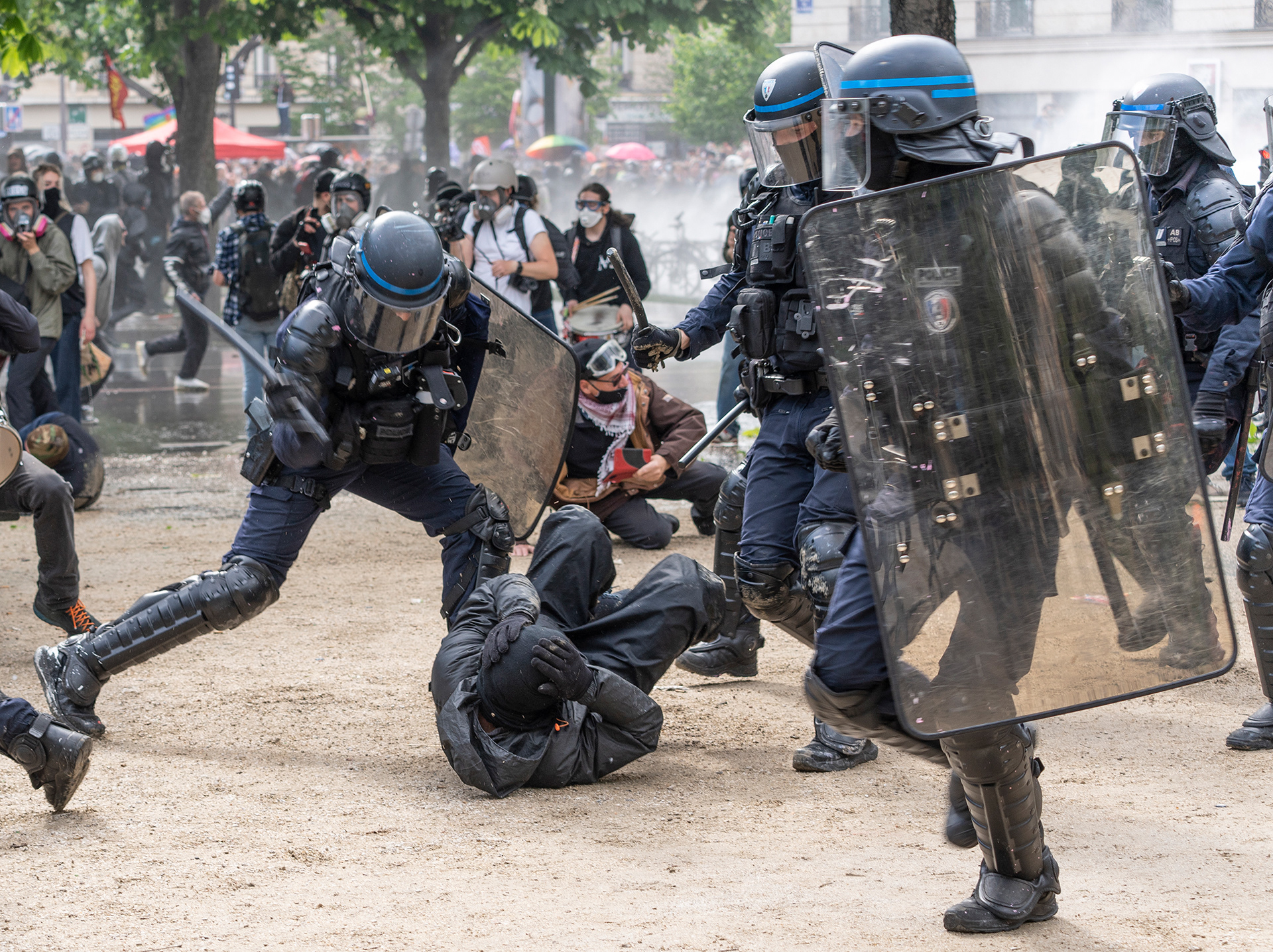 Mehrere Polizist*innen schlagen auf eine auf dem Boden liegende Person ein.
