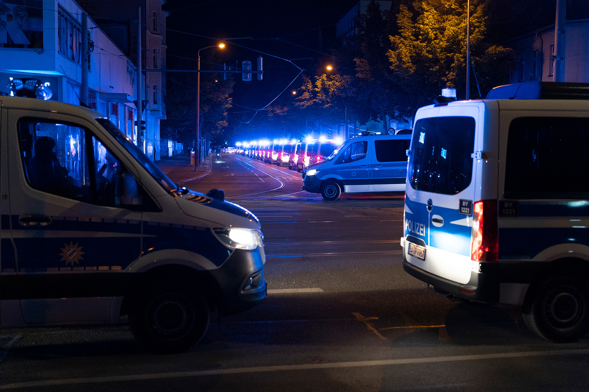 Polizeiautos mit Blaulicht an stehen nachts geparkt am Straßenrand.