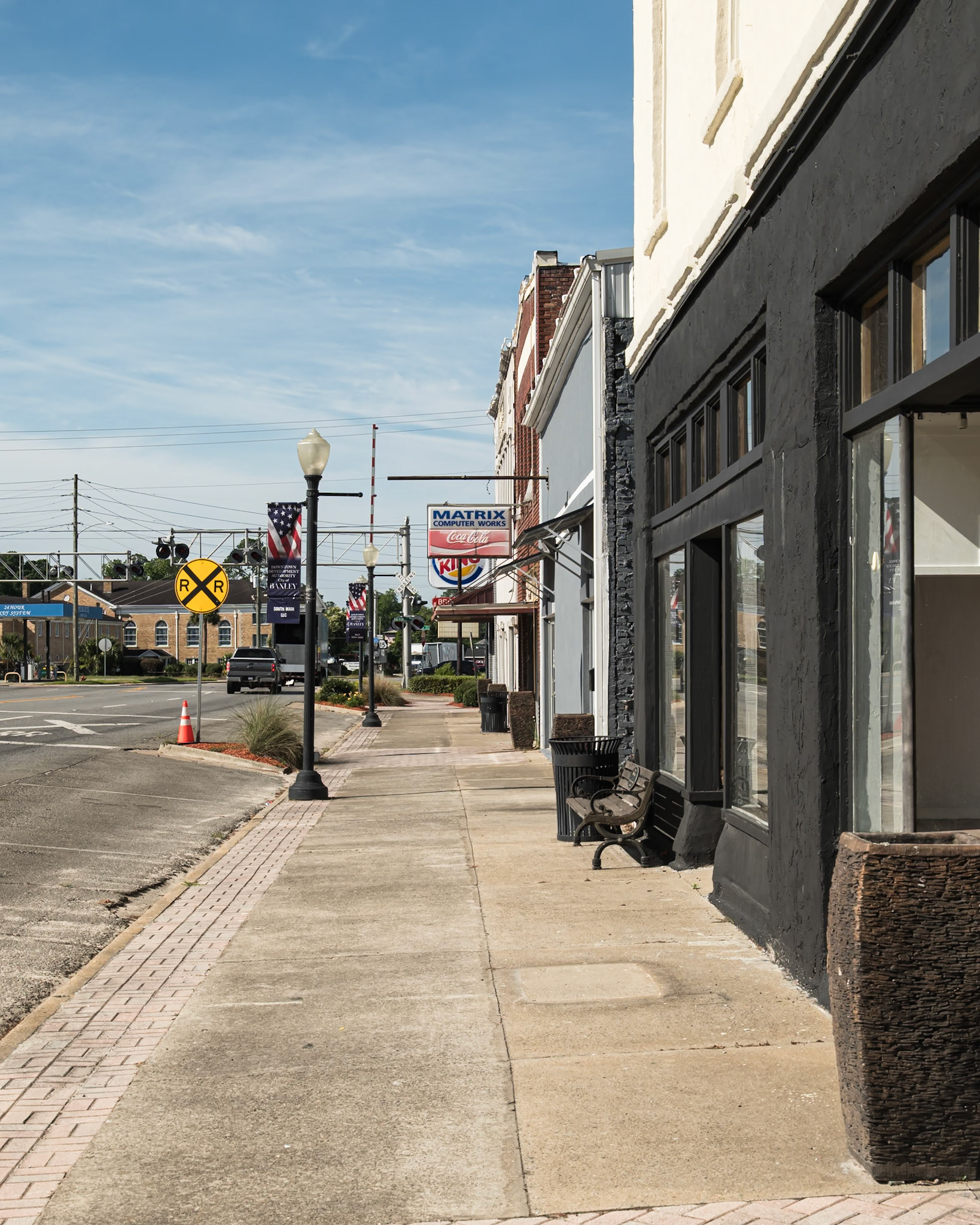 A downtown Baxley sidewalk looking toward the railroad crossing and commercial district, in June 2024