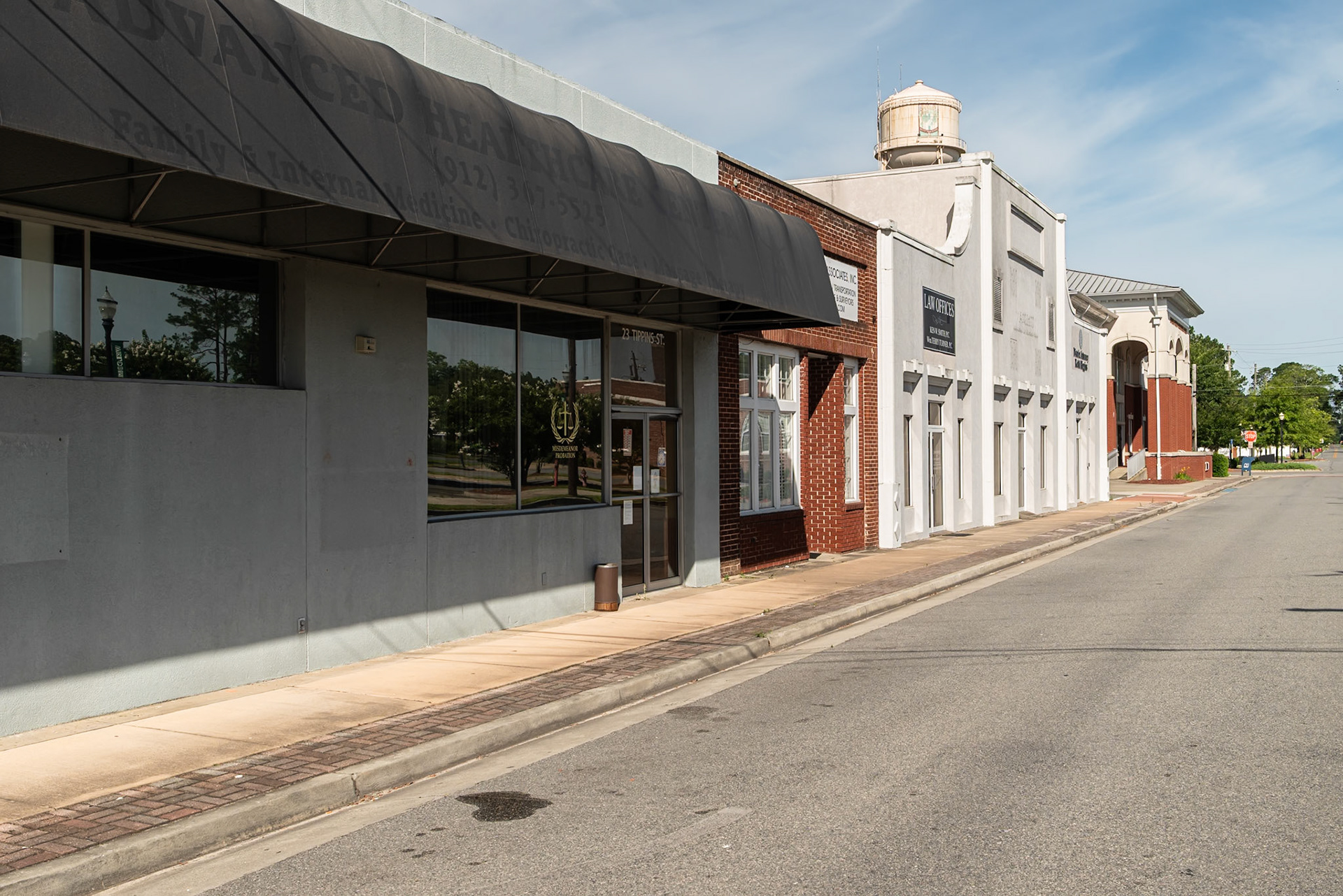 Commercial buildings along a downtown street in Baxley, Georgia, with the city water tower visible above the rooftops, in June 2024