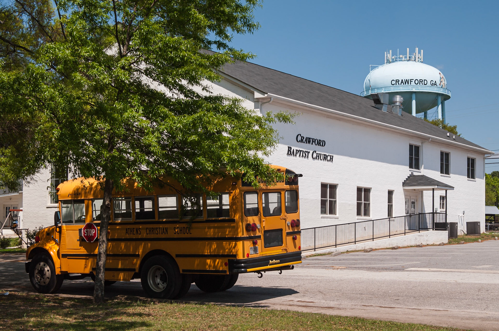 A Crawford Baptist Church building with a school bus and the Crawford water tower in the background, photographed in April 2014