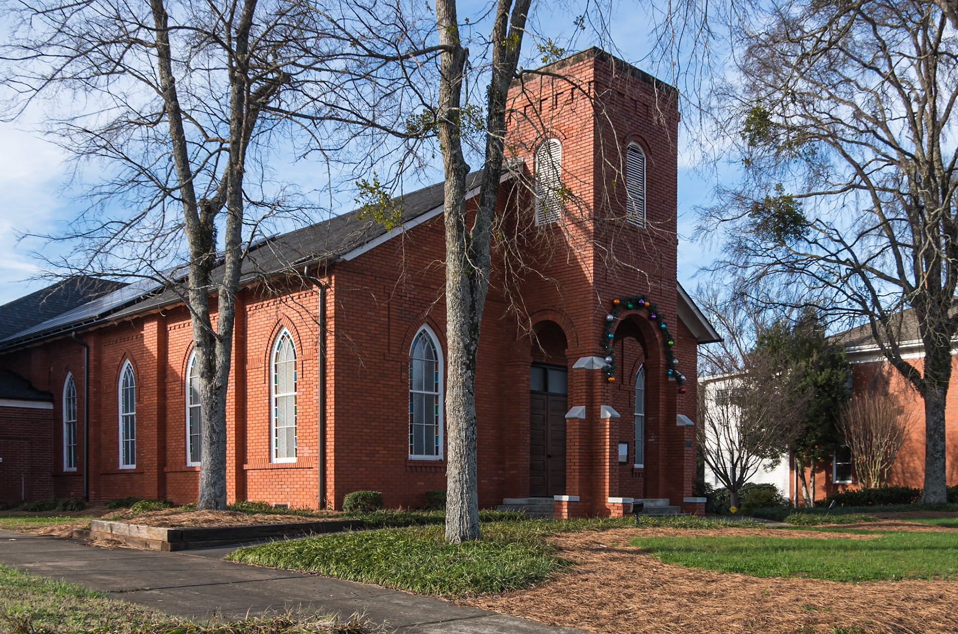 Red brick church with Gothic-arched windows and a square tower framed by large leafless trees