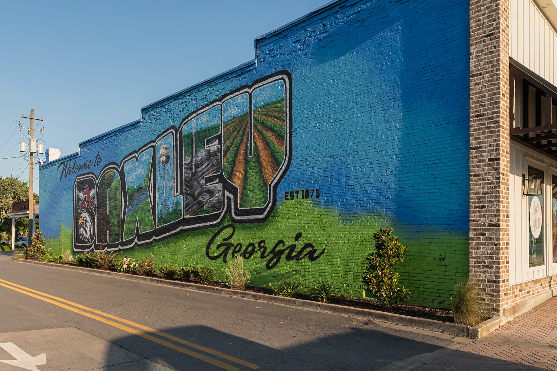 An angled view along the brick wall carrying the Welcome to Baxley mural, in June 2024