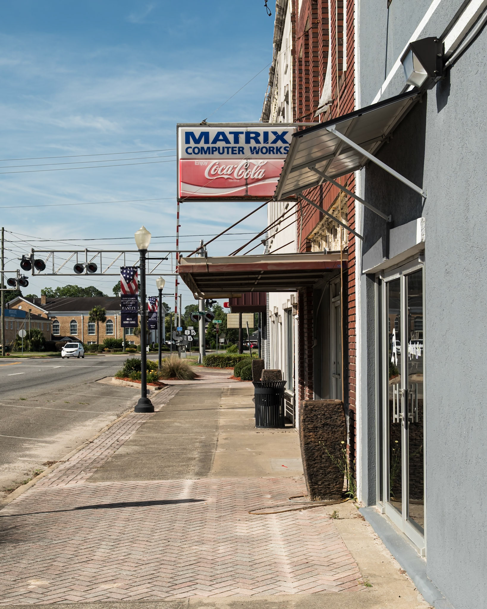 Storefronts, an older projecting Coca-Cola sign, and the railroad crossing in downtown Baxley, in June 2024