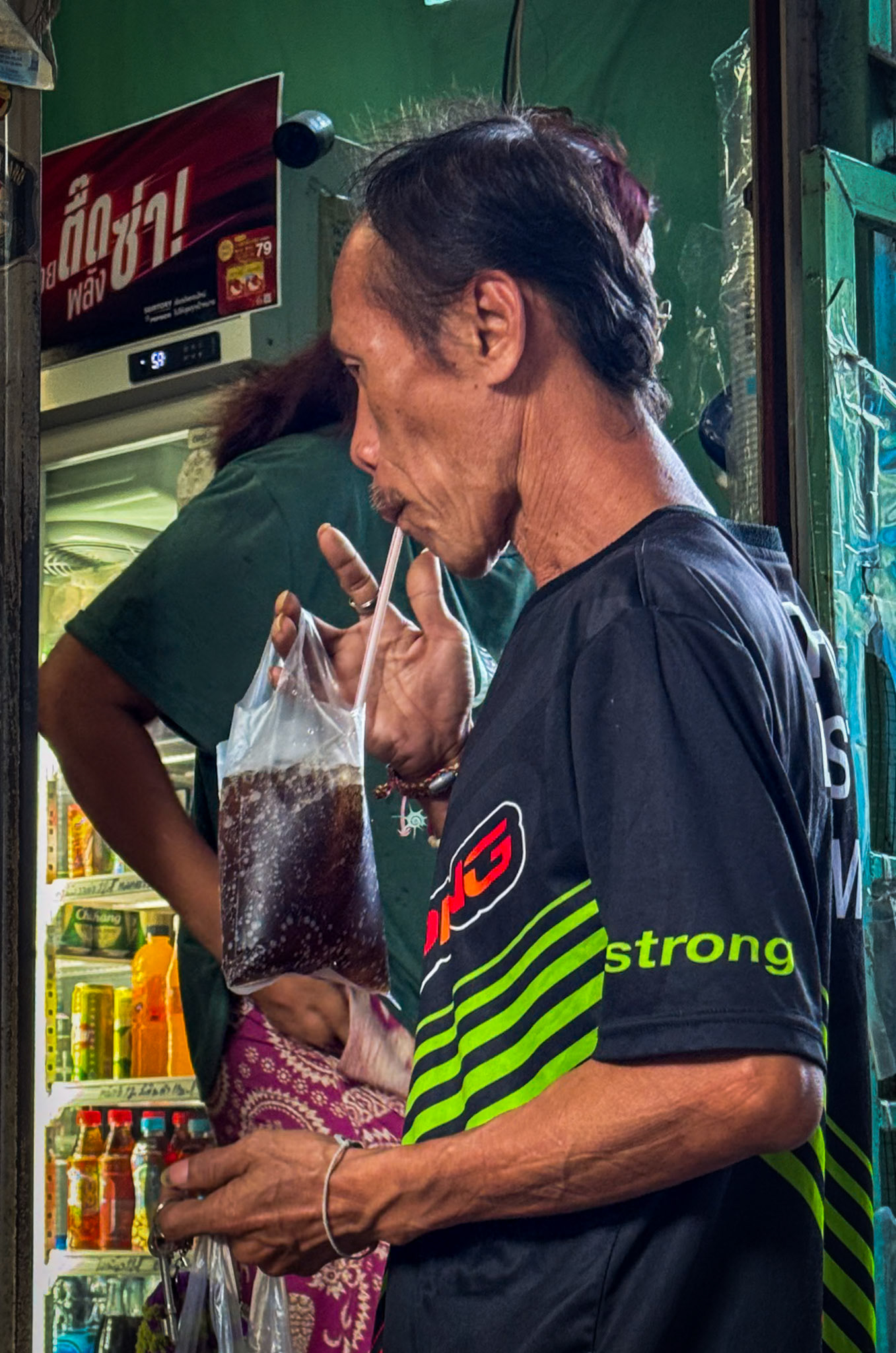 A man, drinking Coke from a plastic bag @ Khlong Toei Slum, Bangkok, Thailand