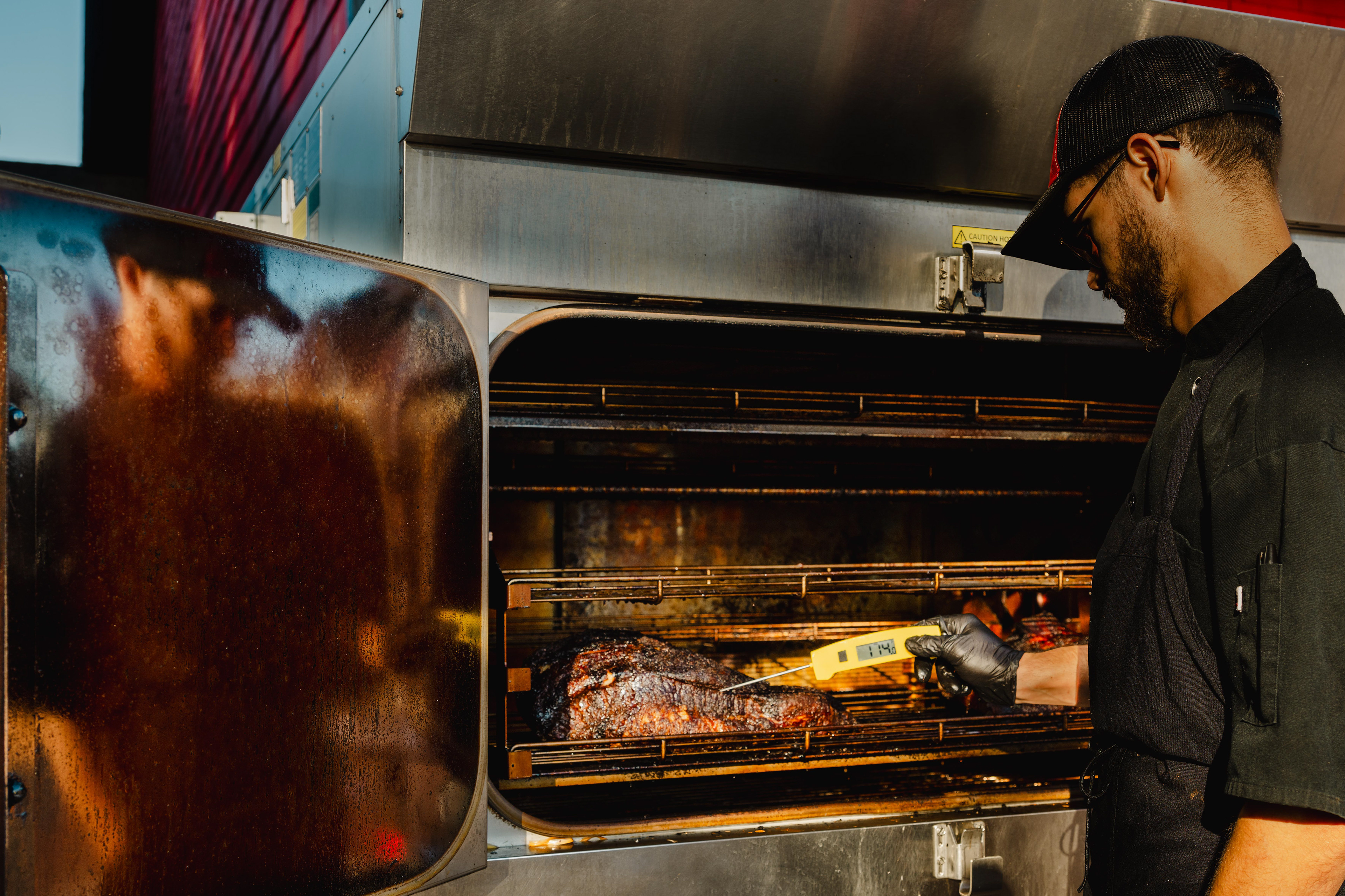 Chef Dawson Gilbert checks the brisket temperature to ensure it reaches 200 degrees Fahrenheit for optimal tenderness and texture at the Angry Smokehouse in Baldwinsville, NY.