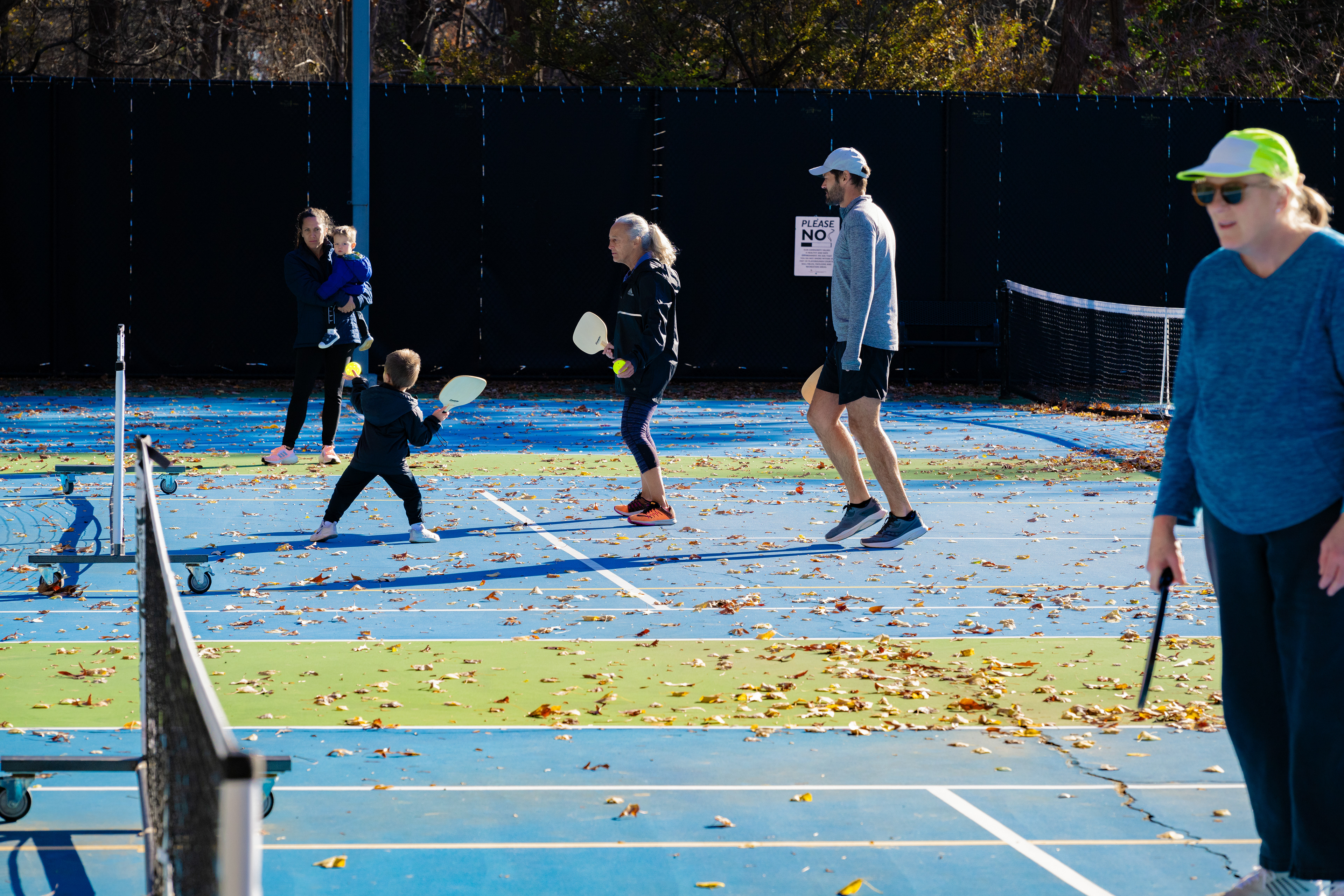  A family bonds over a lively game of pickleball on a sunny court covered with autumn leaves in Virginia. As one of the fastest-growing sports for all ages, pickleball brings people together while promoting health, fitness, and community connection.