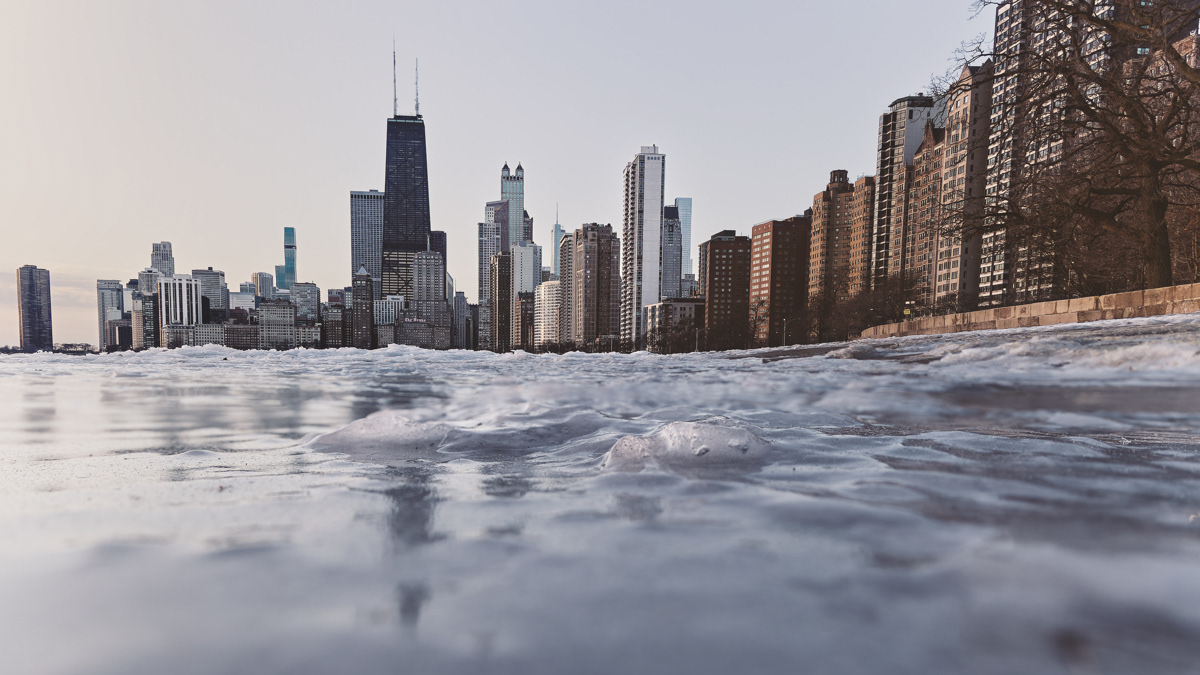 Ice covering North Avenue Beach on Chicago's Lakefront with a view of the John Hancock Building and the Chicago skyline in the background.