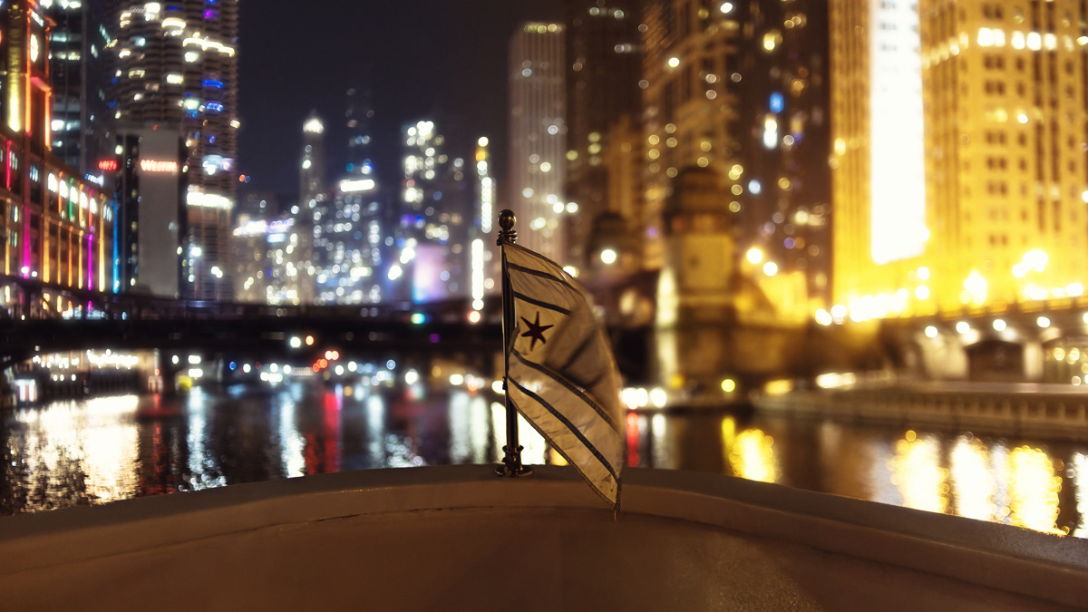 Chicago flag blowing in the wind from a boat on the Chicago River at night.