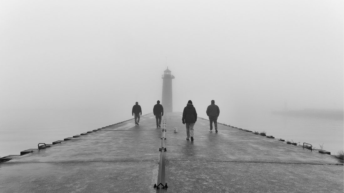 Black and white photo of 4 people walking towards Kenosha North Pier Lighthouse into the fog.