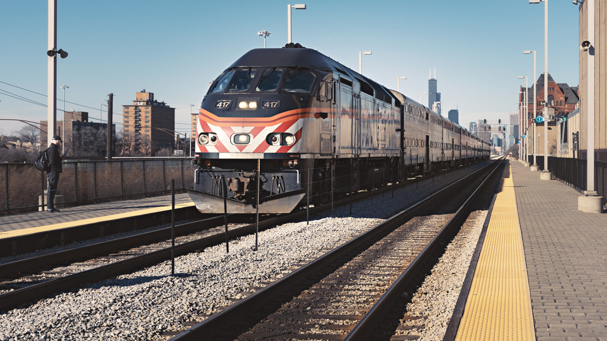 Metra train on a track near White Sox staduim with Chicago skyline in the background.
