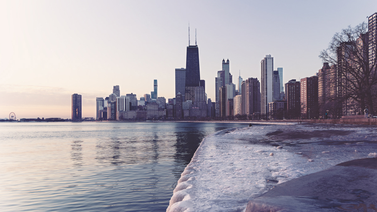 Snow covering the boardwalk on North Avenue Beach on Chicago's Lakefront with a view of the John Hancock Building and the Chicago skyline in the background.