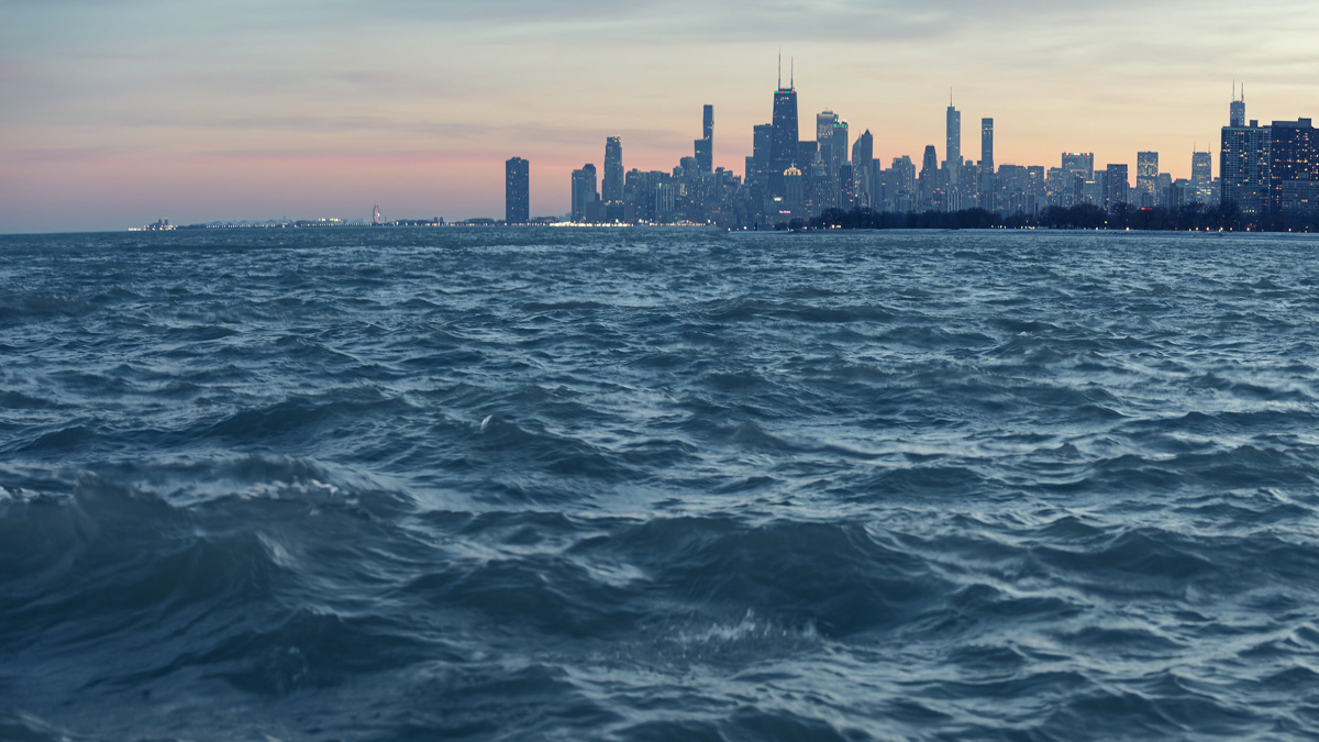 Rough waves on Lake Michigan contrast with a serene view of the Chicago skyline at sunset from Montrose Harbor.