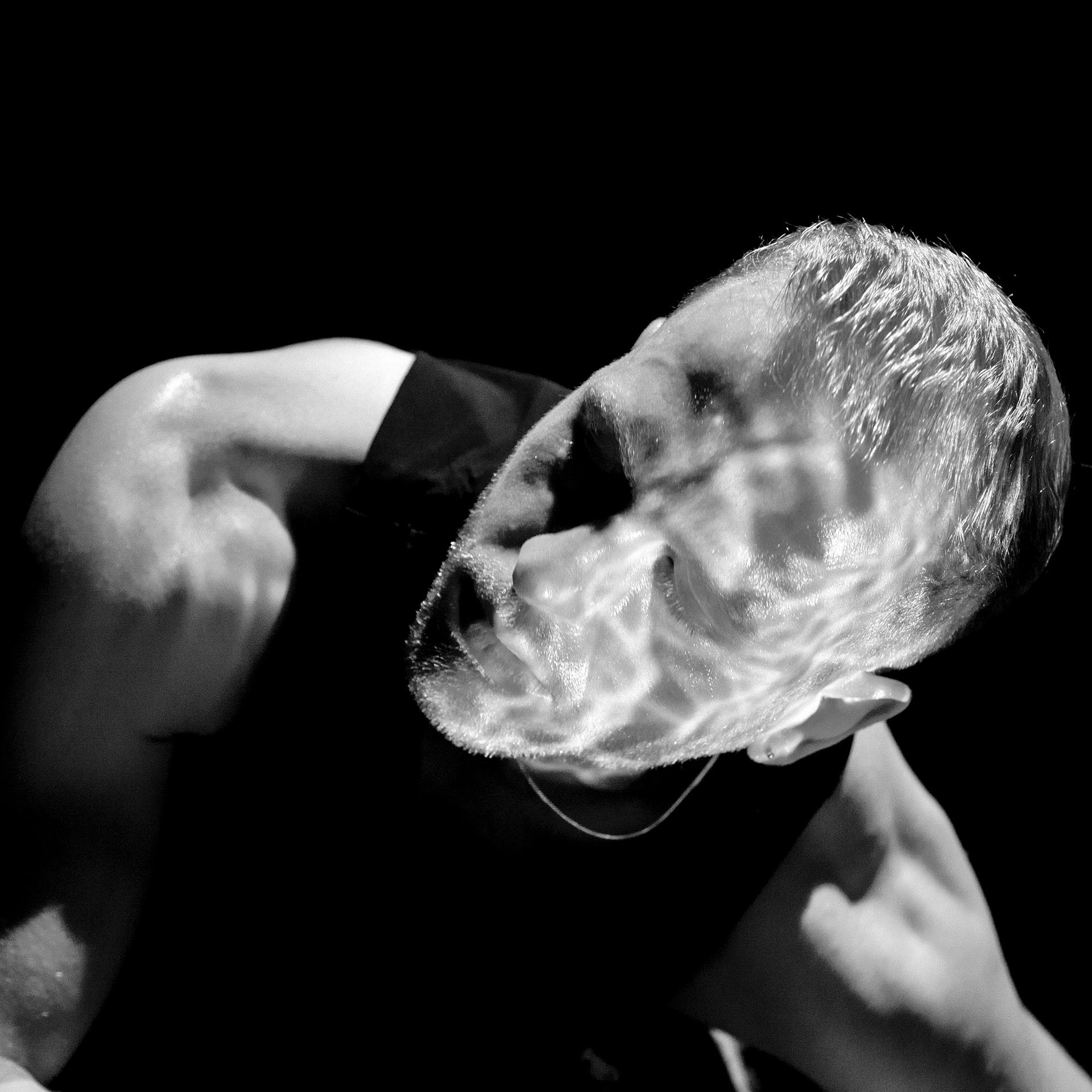 A white person contorts their head to one side as rippling water reflects on their body.