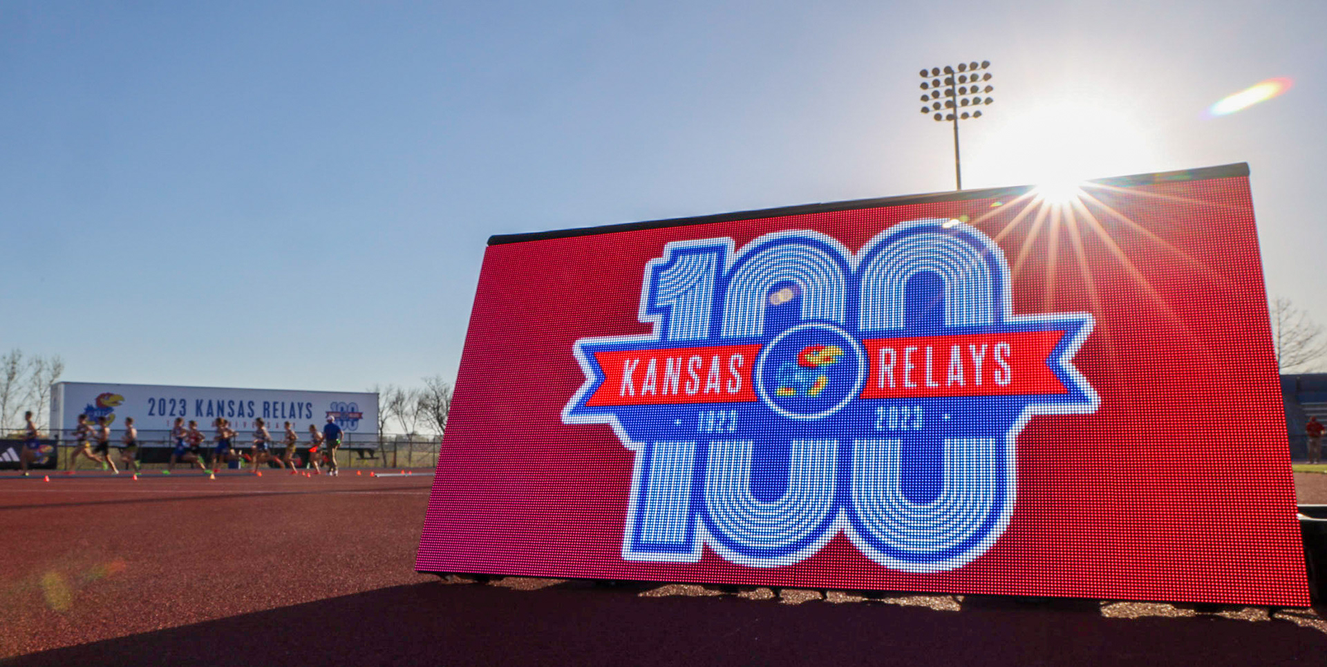 Racers in the men's 800 meter race sprint past the 100th anniversary of the Kansas Relays sign in Lawrence, Kan. April 13, 2023.
