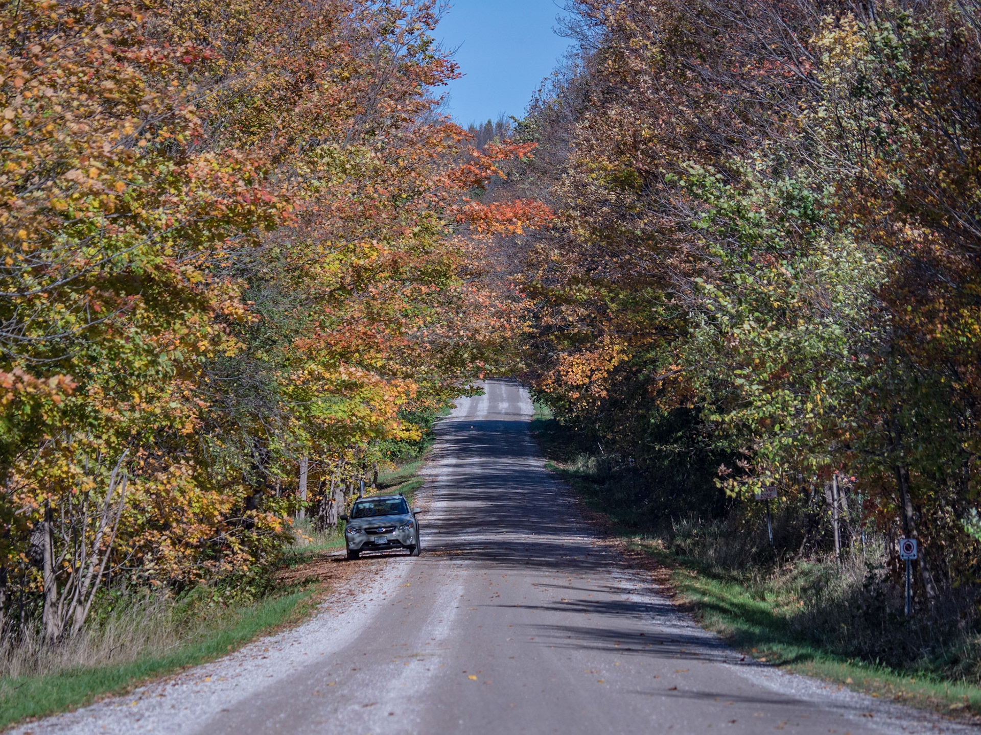 A lone car is parked at the side of a country road on a sunny fall day in Ontario.