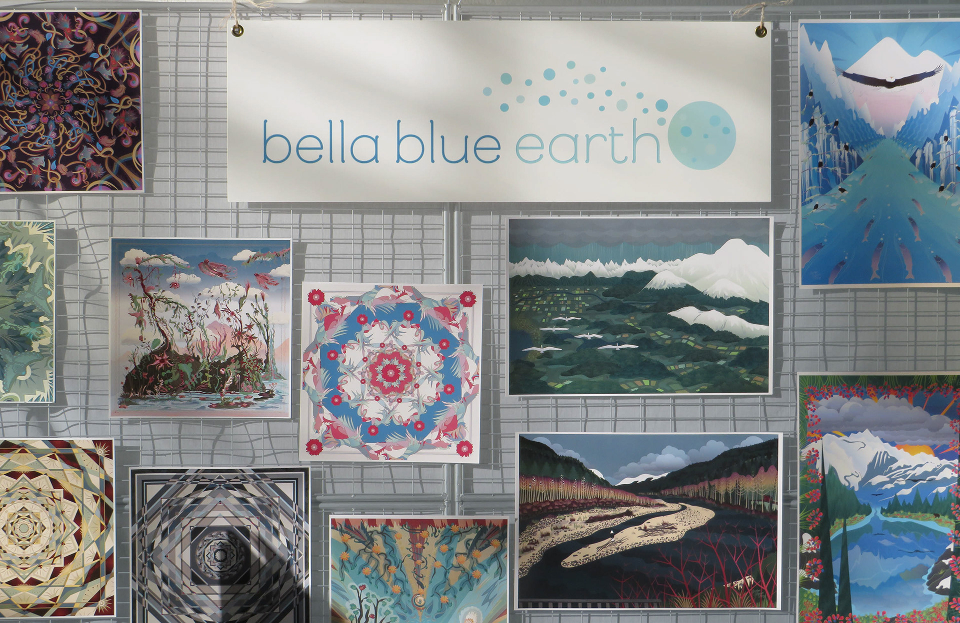 Art posters hung on a display with nature and mandala designs below a sign that says Bella Blue Earth.