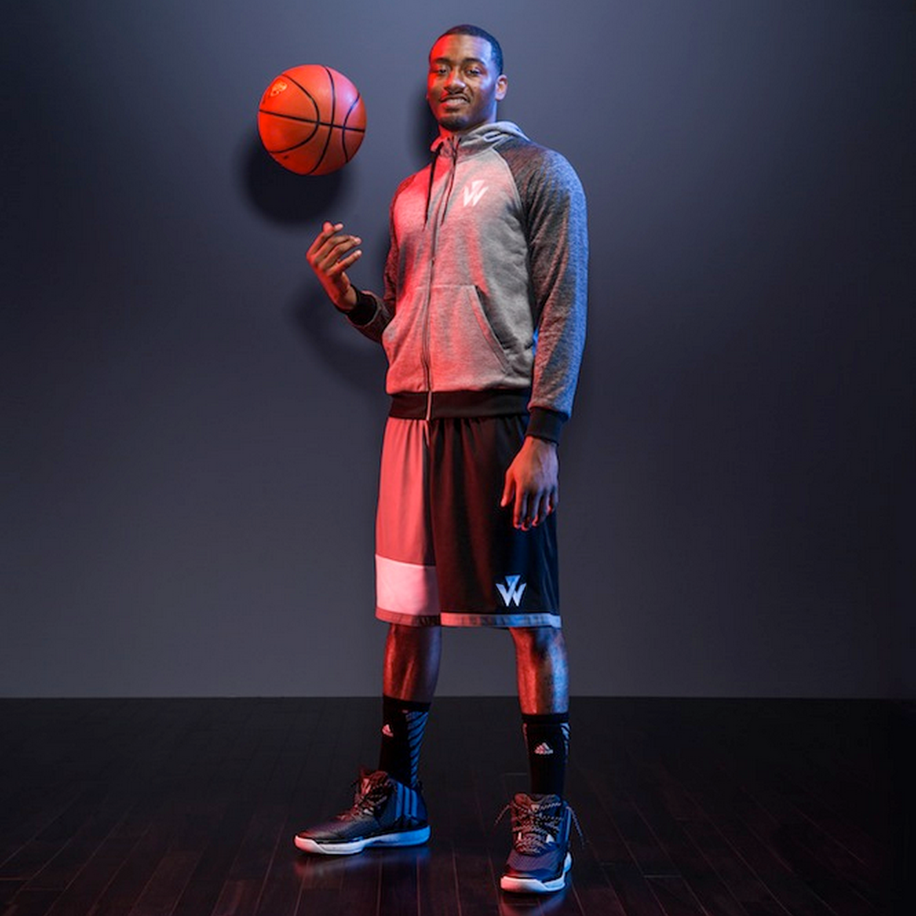 Photograph of John Wall tossing up a basketball in the air while wearing hoodie, shorts and shoes.