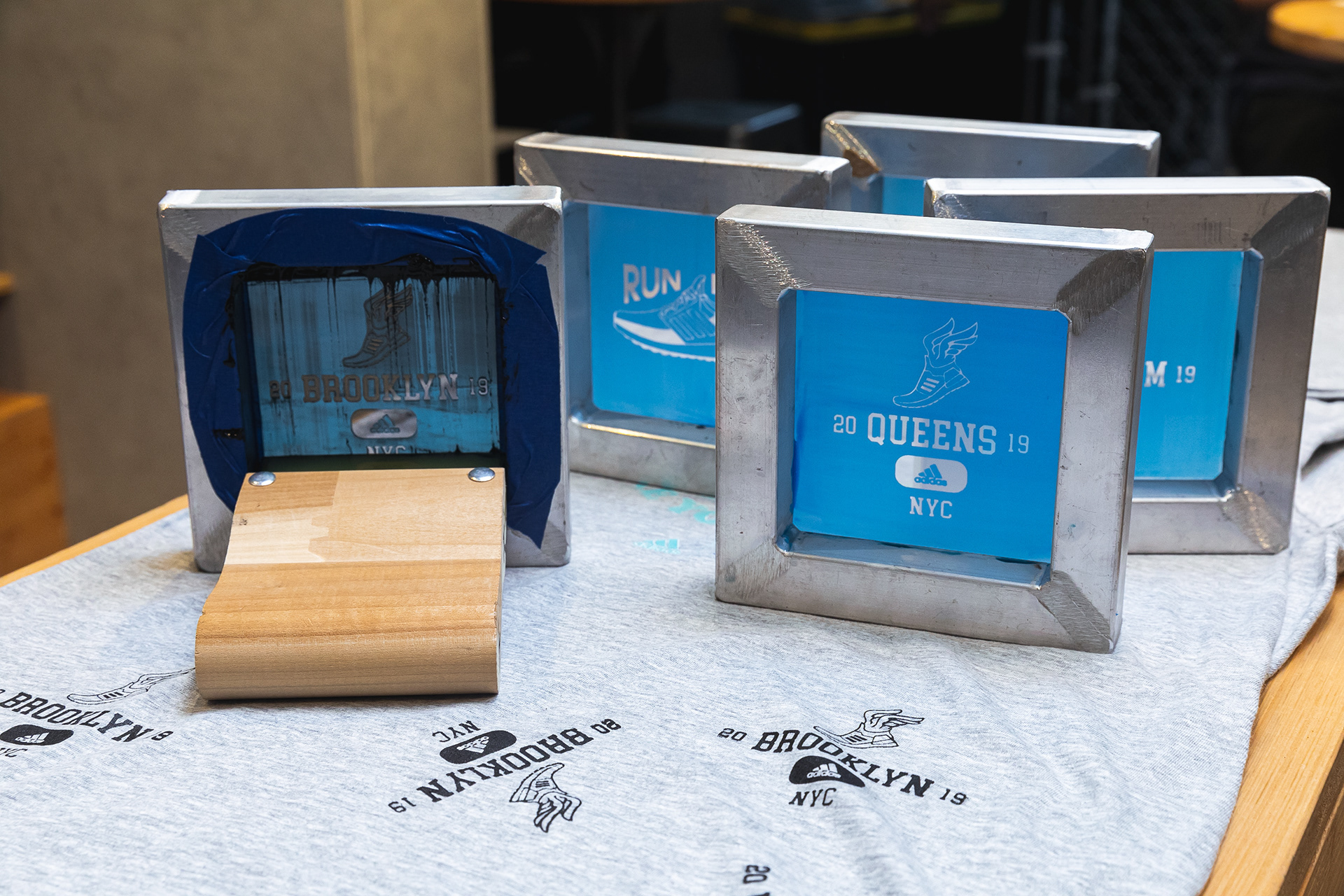 Photograph of small screenprinting screens freshly inked on t-shirts featuring graphics of the NYC boroughs.