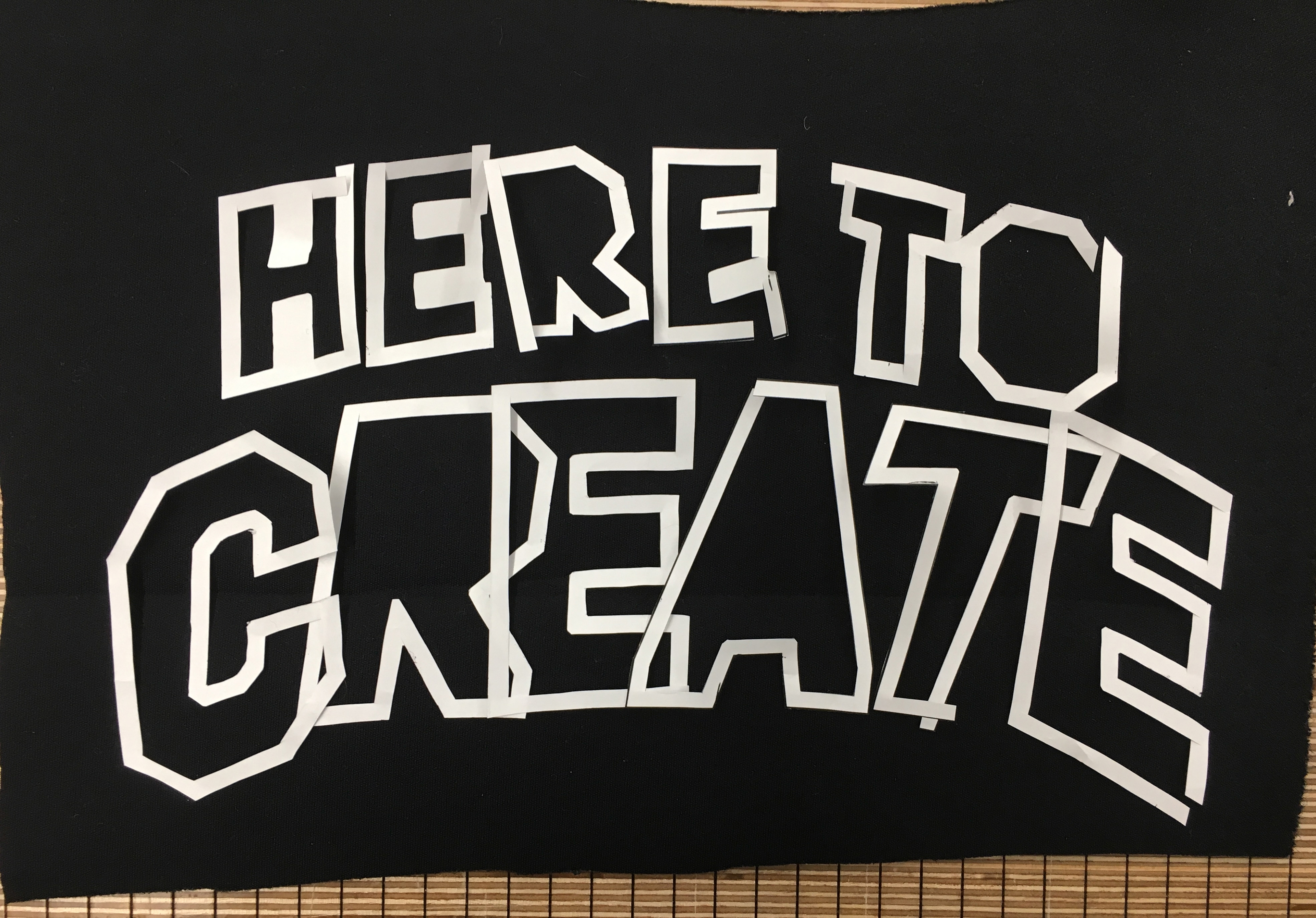 Photograph of "Here to Create" outline of letters cut-out from paper.
