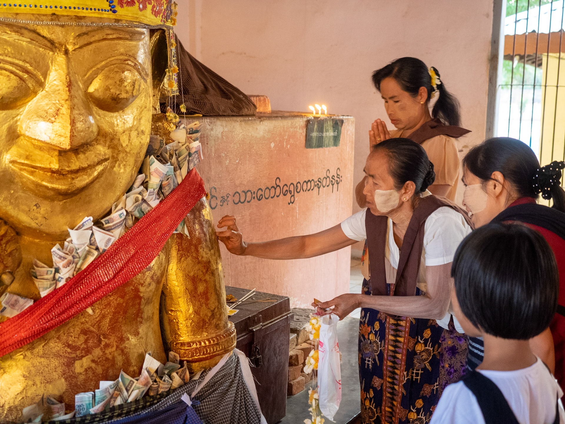 Visitors give many offerings in the temples. It could be candles, flowers, water (to refresh Buddha statues outside) or money donations. Here, it’s another kind which is applying a piece of gold leaf to a Buddha statue. In this case it’s a Nat, which is a spirit and not a Buddha god.