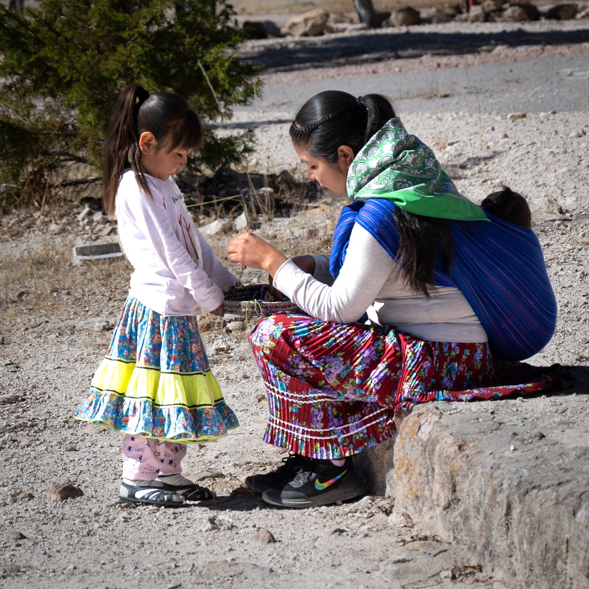 Her mom is carrying her baby the traditional way, draped on her back.