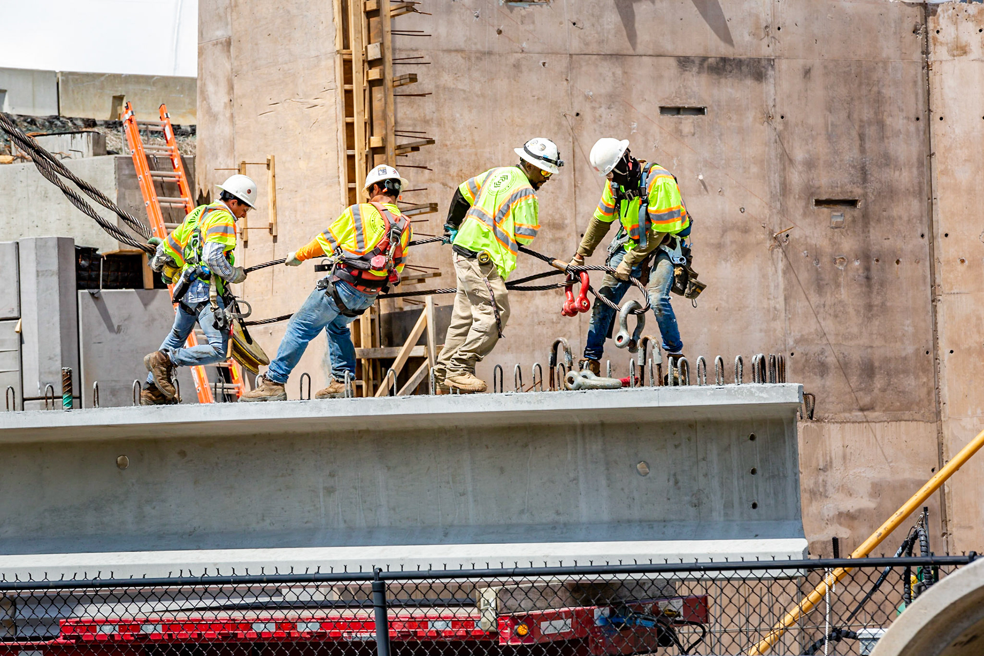 Construction workers on I-beam pulling massive steal cable, Belmont bridge construction