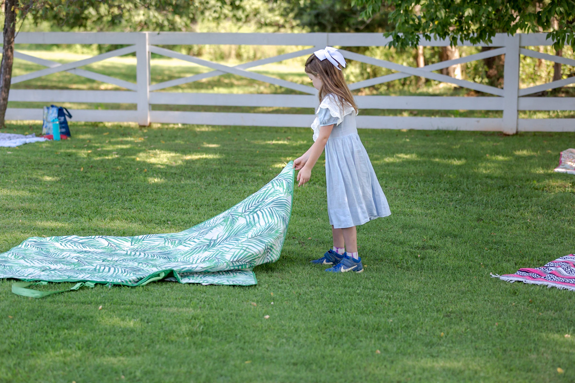 A young girl spreading a picnic blanket on the grass