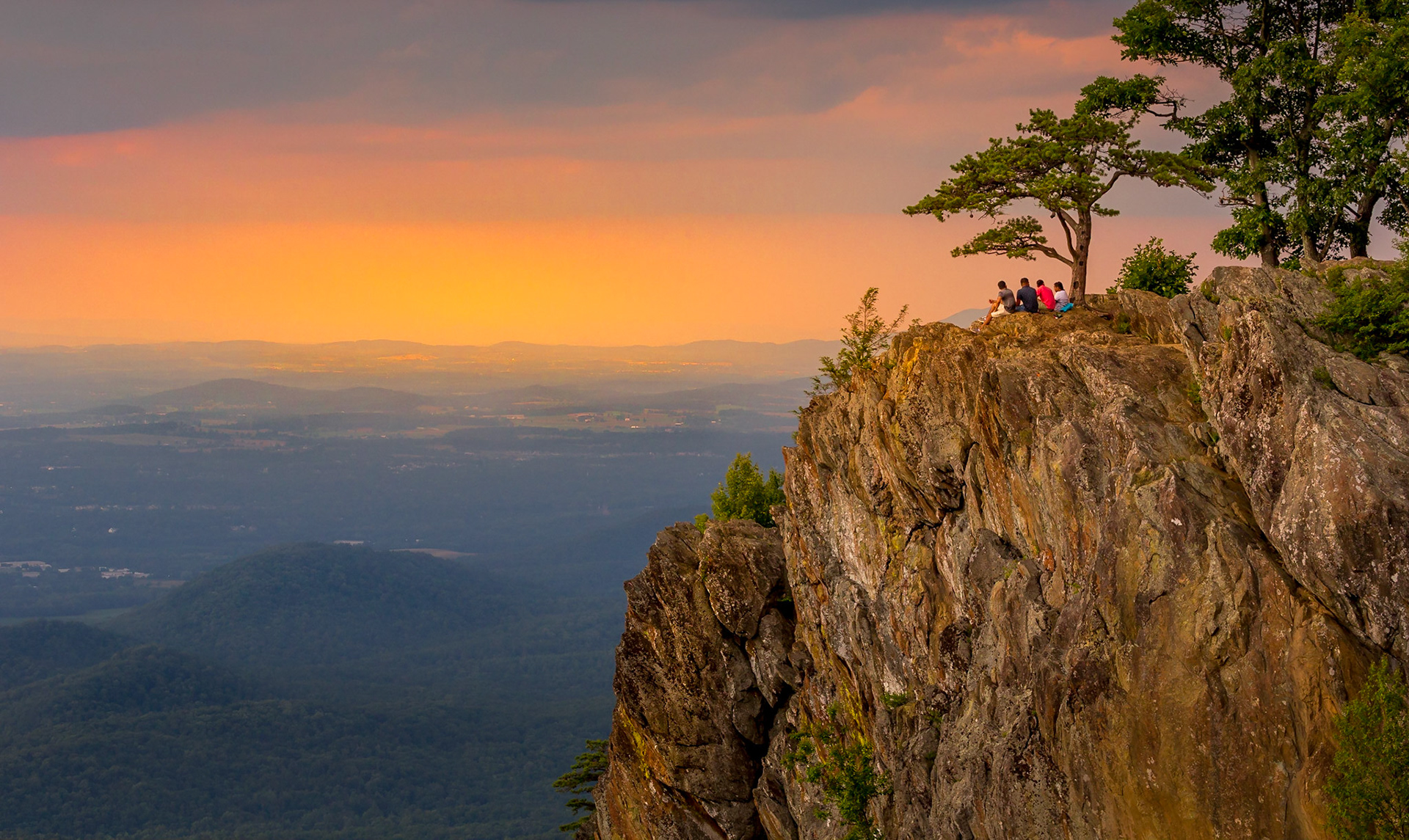 Four people sitting on a cliff watching a gorgeous sunset over the Shenandoah Valley
