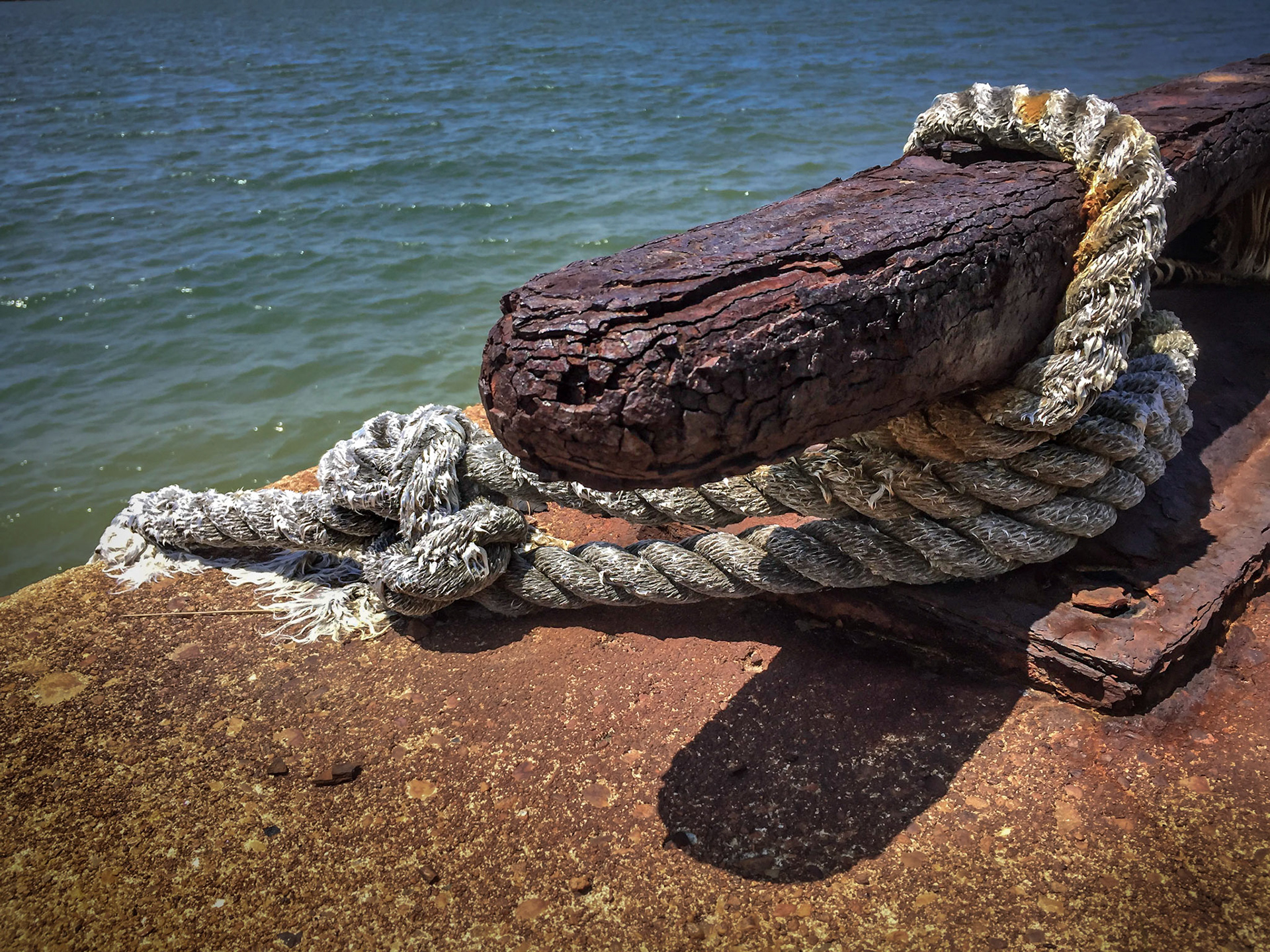 Large cleat slowly rusting away with a deteriated rope attached