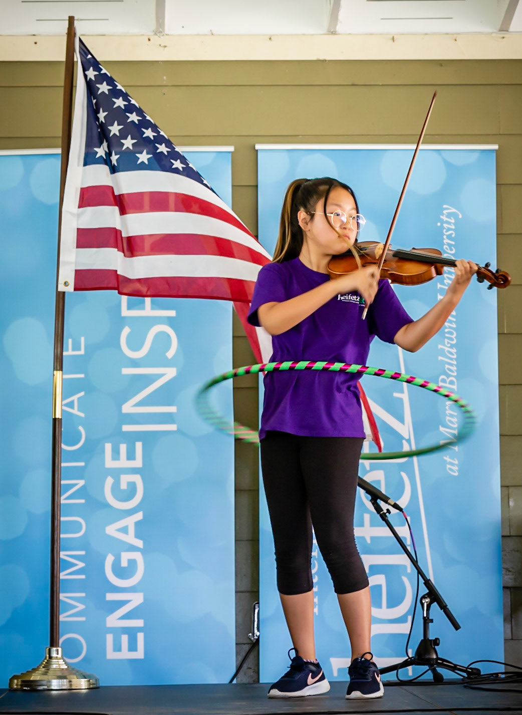 Gifted music student from the Heifetz International Music Institute performing with a hula hoop and playing the violin on stage next to the American flag