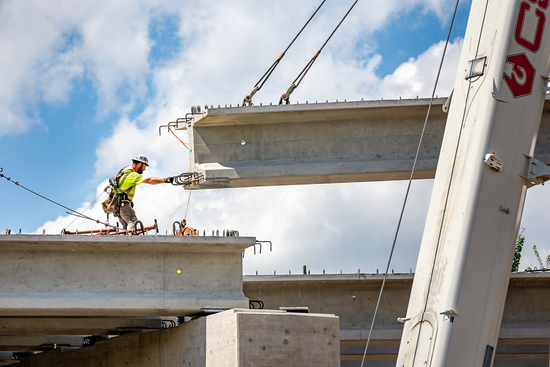 Workmen guiding a large I-beam being lifted into place for the new Belmont Bridge.