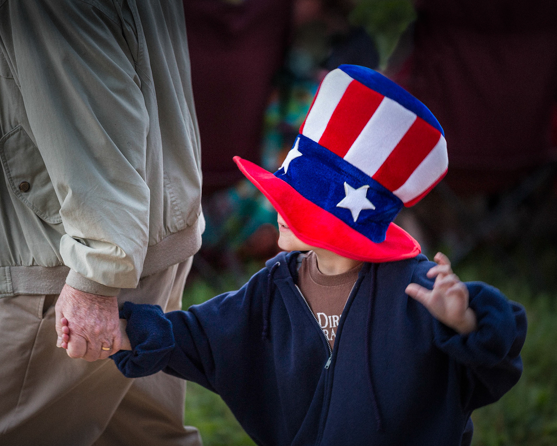 Grandad Leading his grandson with large red, white, blue hat on the 4th of July