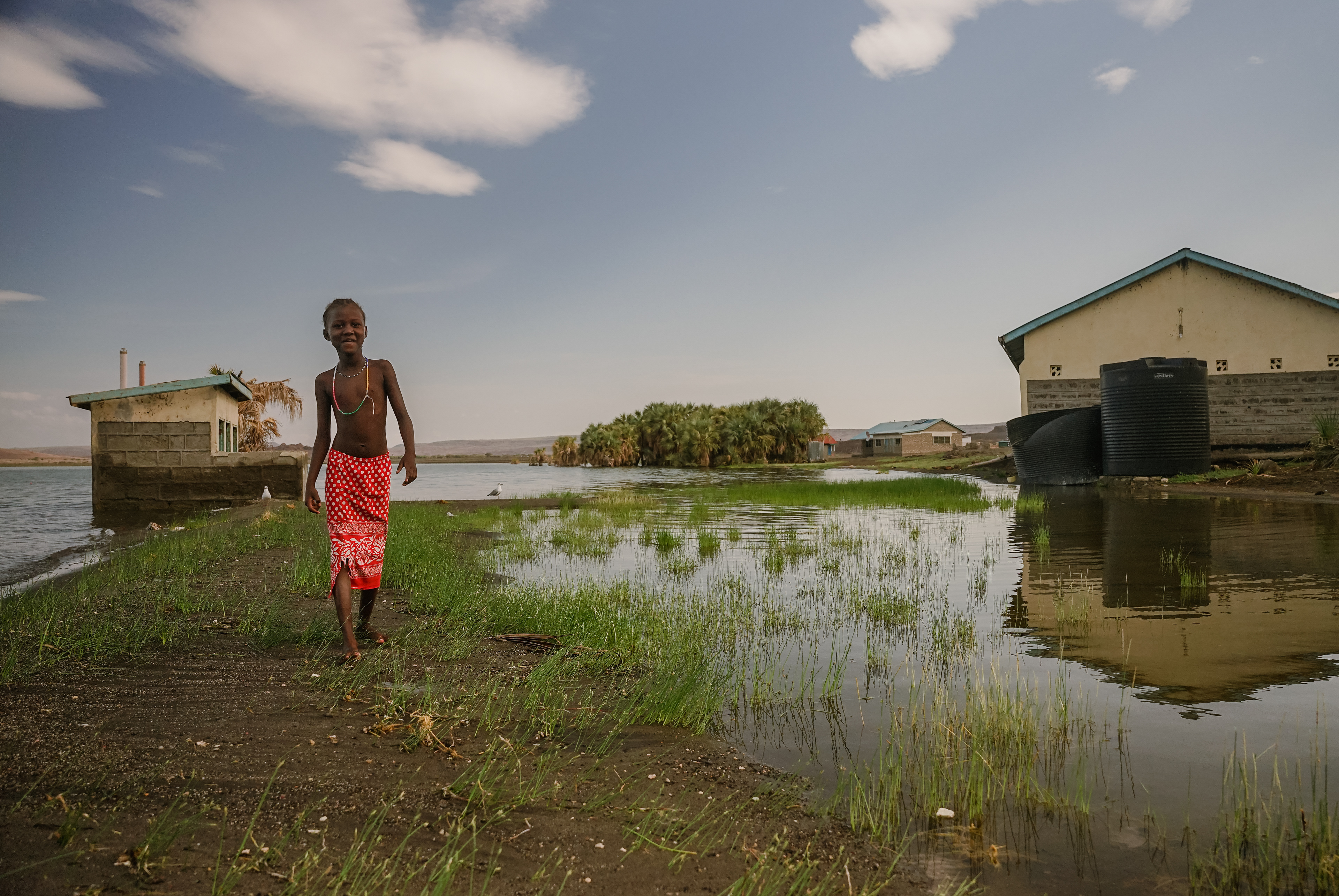 An El Molo girl walks next to what is left of the school toilet, now flooded from rising lake water levels